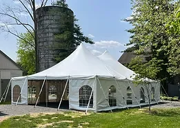 Large white event tent set up outdoors on grass with trees and a silo in background.