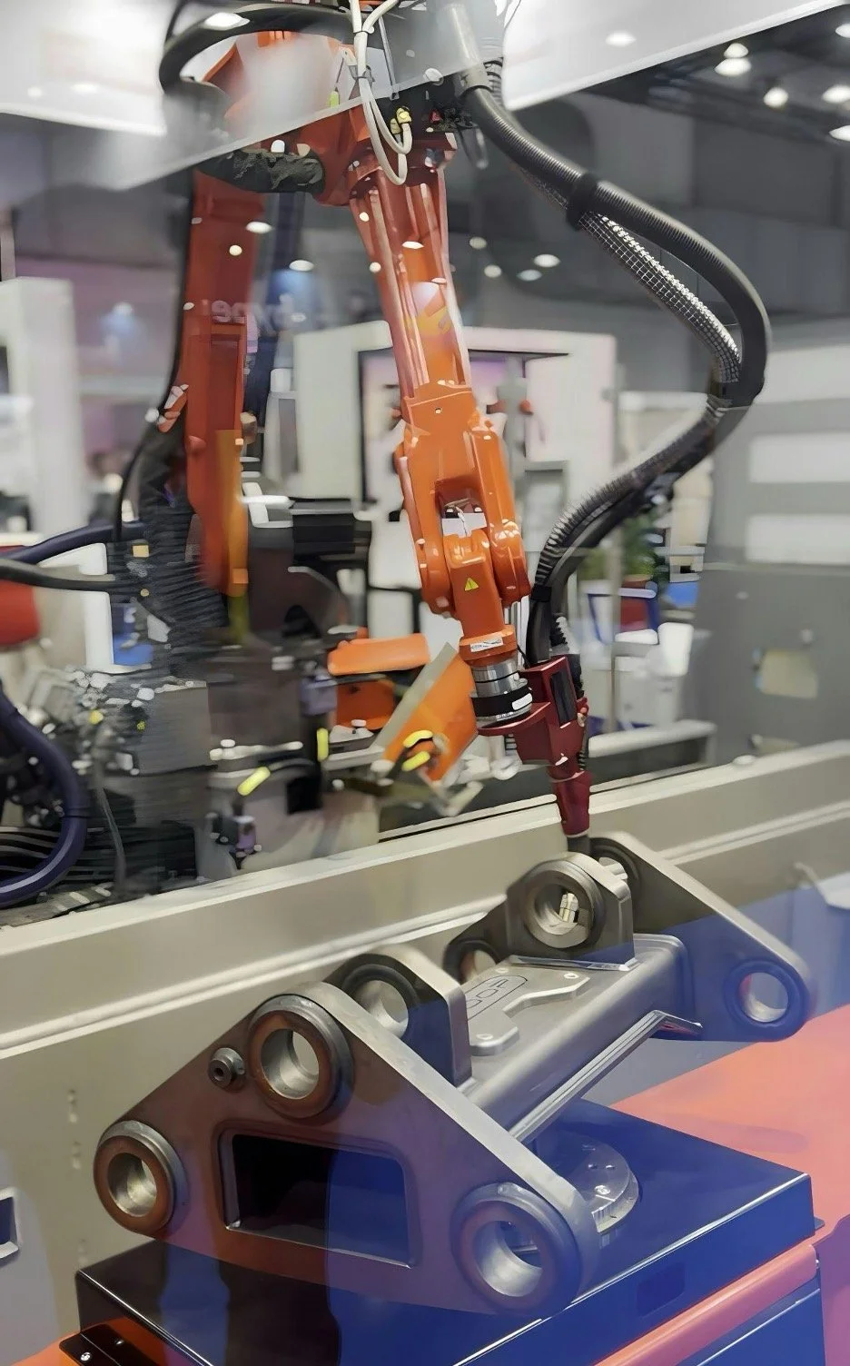 Close-up of a robotic arm with orange and red components operating in a manufacturing or assembly environment.