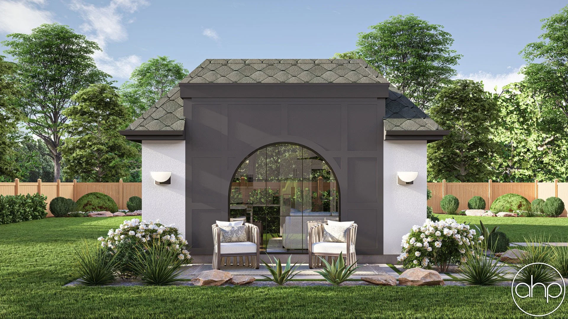 Backyard scene featuring a small modern building with gray panels and a arched window reflection, surrounded by green lawn, shrubs, flowers, and tall trees, with a wooden fence in the background.