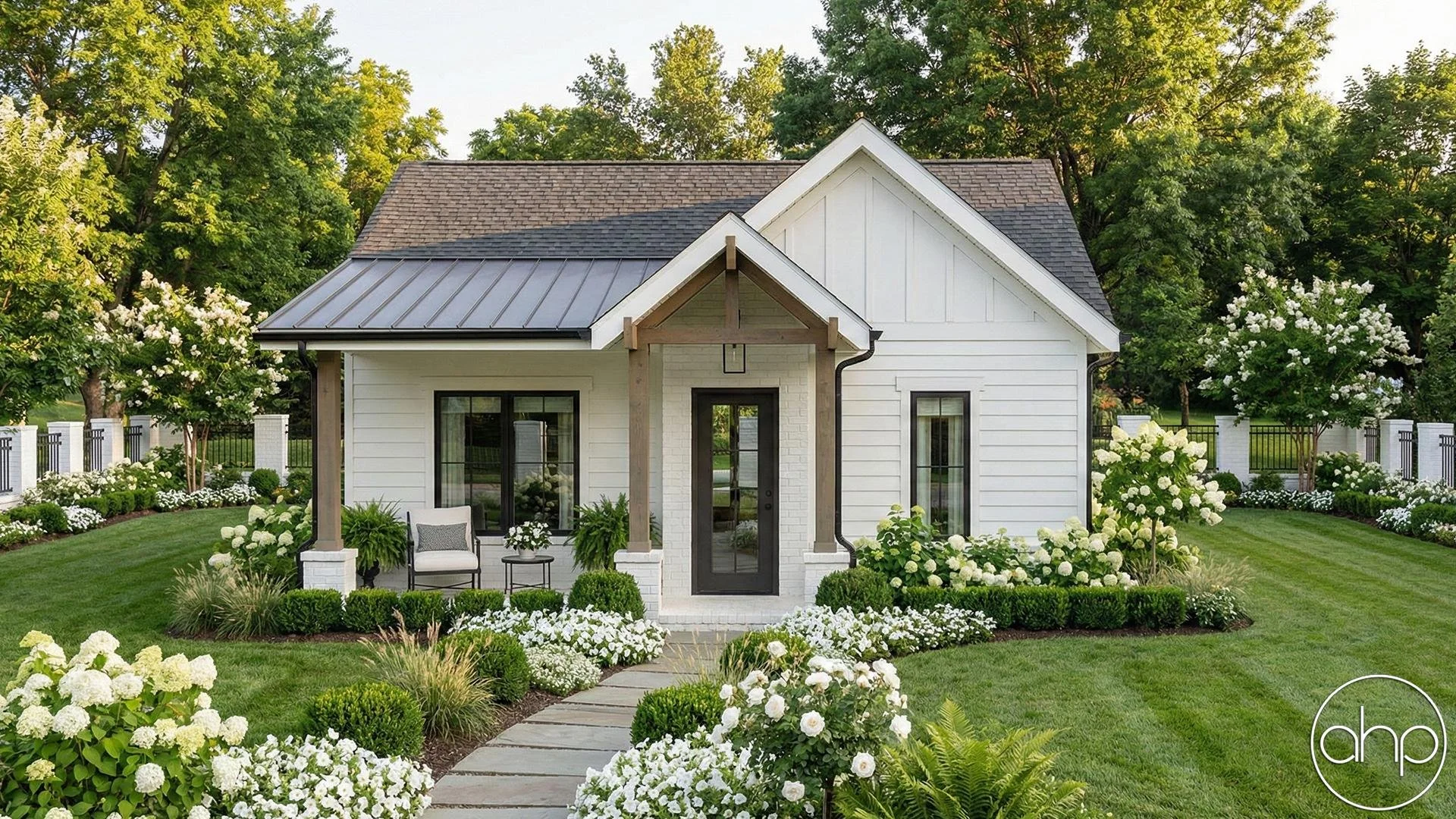 A charming white house with black accents, surrounded by a lush well-manicured lawn and vibrant white flowers, with trees and a white fence in the background.