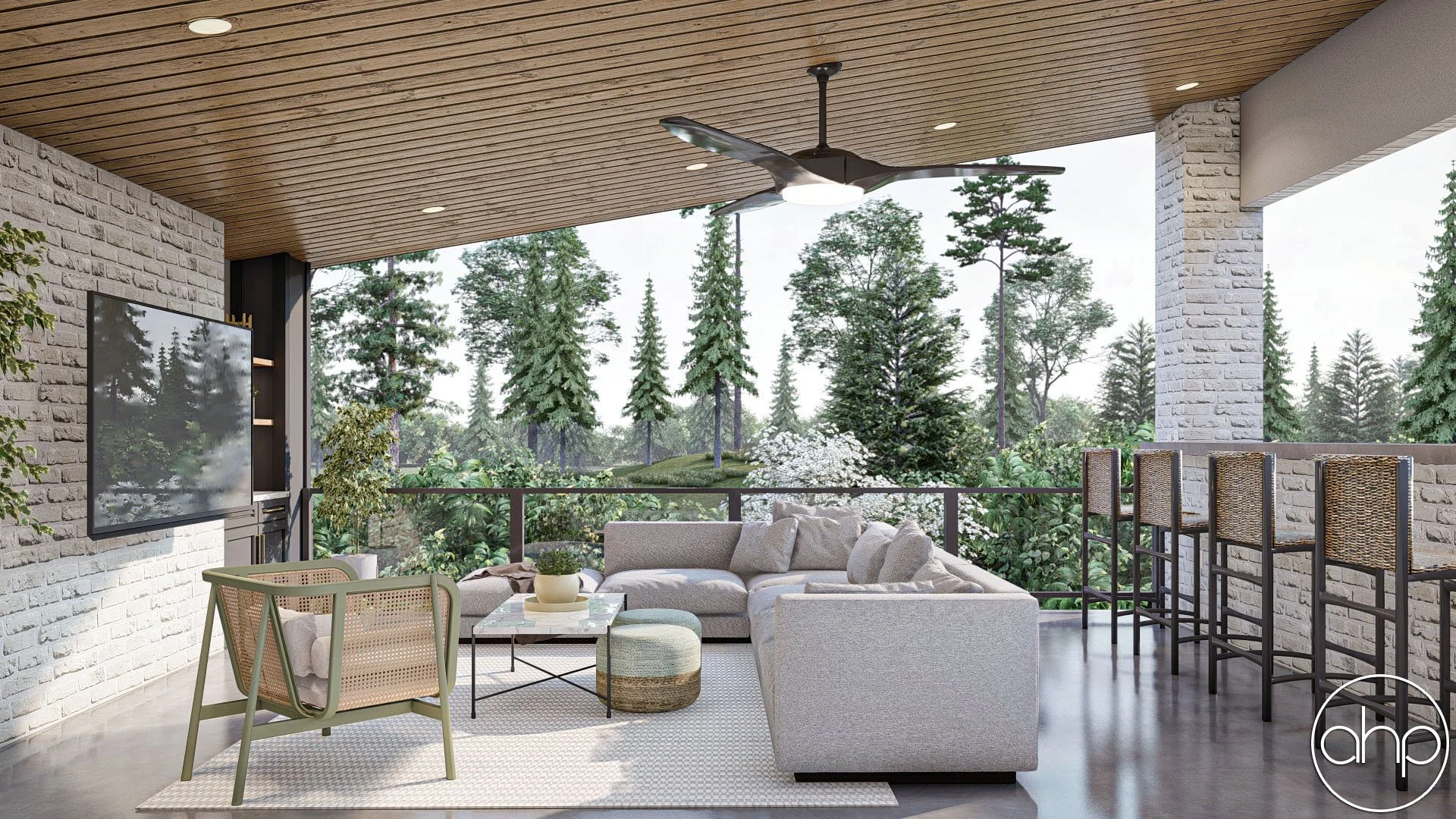 Modern outdoor balcony with white brick walls, wooden ceiling, ceiling fan, large gray sectional couch, armchair, glass coffee table with plant, bar stools, and lush green trees in the background.