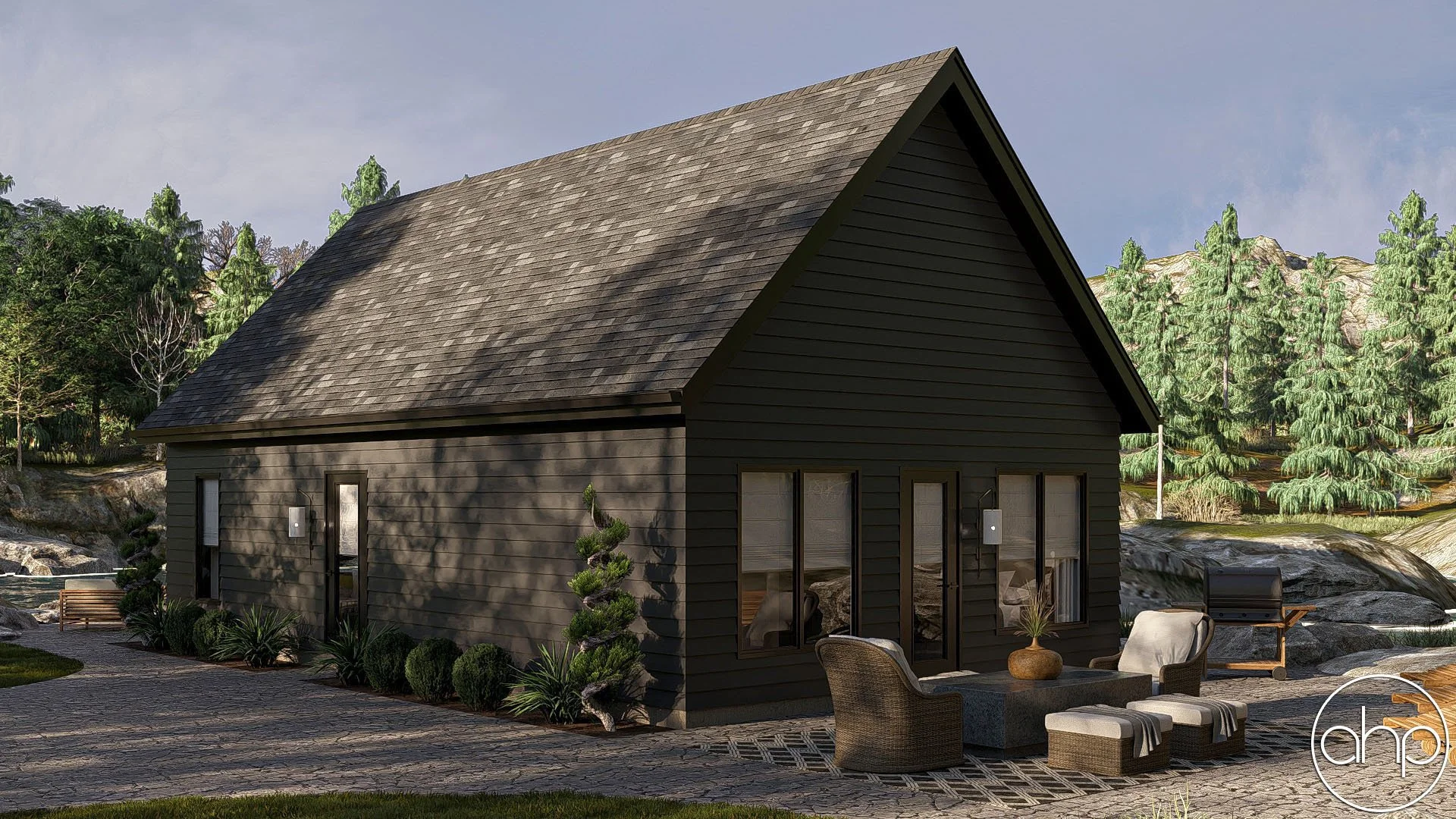 A black wooden house with a large gray shingle roof, situated outdoors with green trees and rocks in the background. The house has large windows and a patio with outdoor seating including chairs, a table with a plant, and a grill.