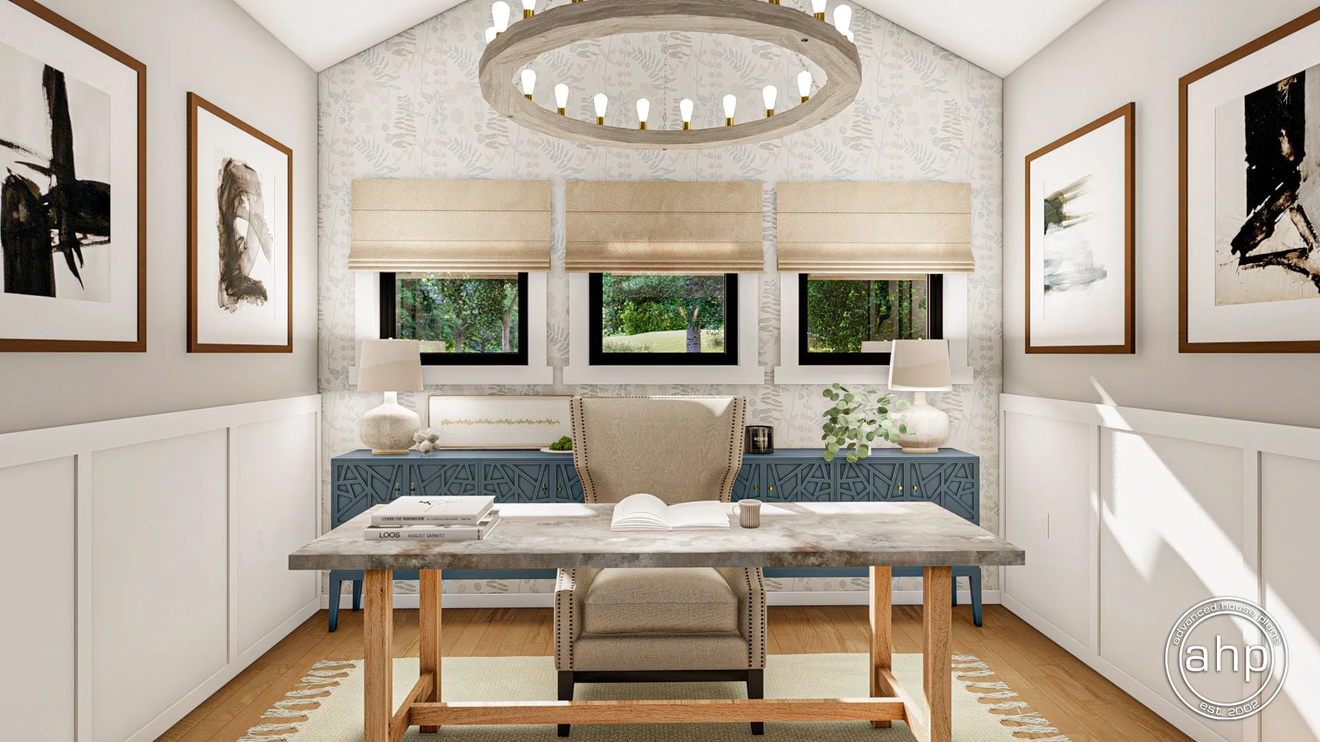 A home office featuring a wooden desk with a beige upholstered chair, three windows with beige blinds, abstract black and white artwork framed on white walls, symmetrical table lamps on blue sideboards, and a circular chandelier with exposed light bulbs.