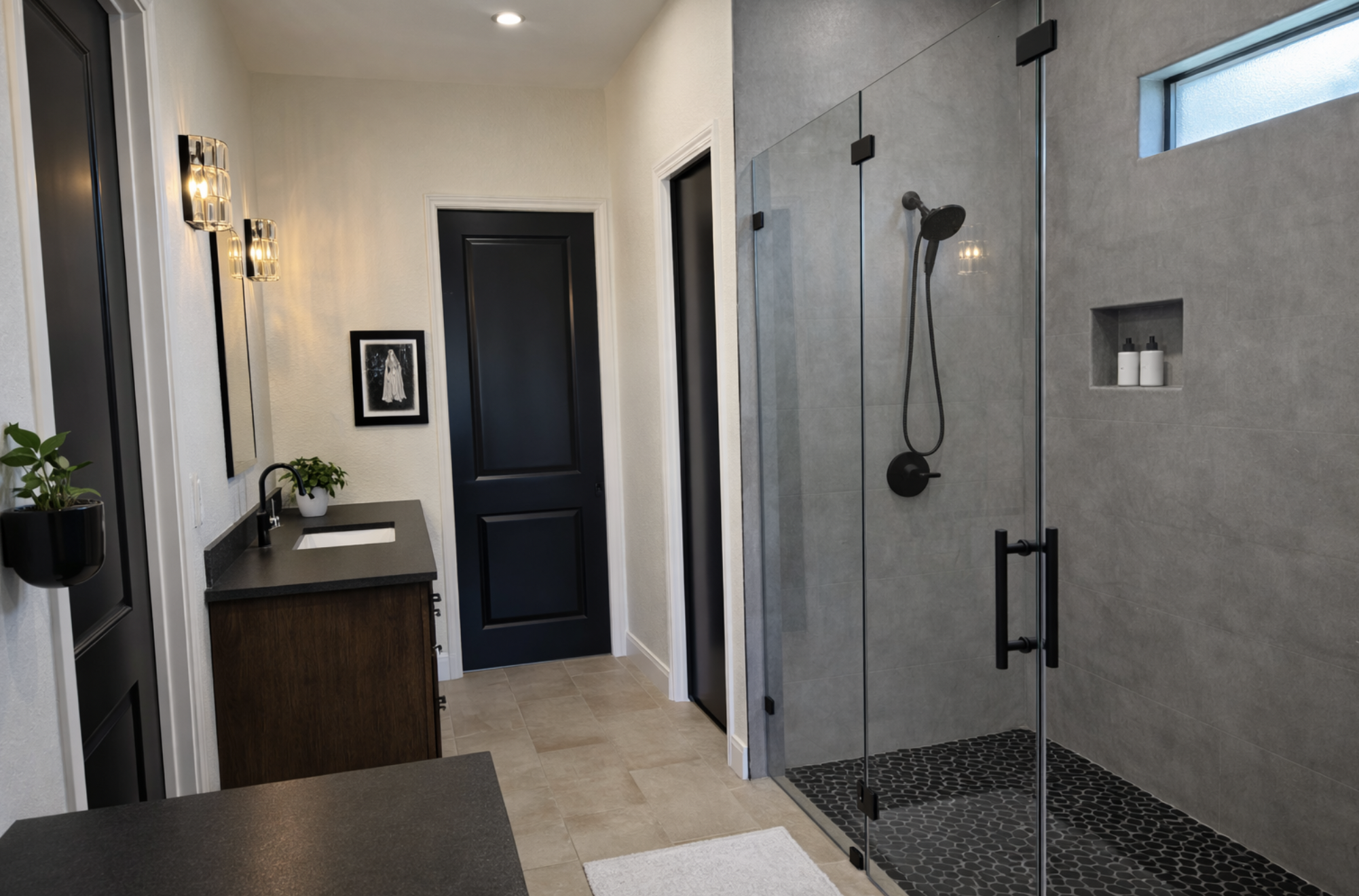 Modern bathroom with black and gray accents, featuring a glass shower with black hardware, a black vanity with a white sink, black-framed mirror, wall sconces, and black doors.