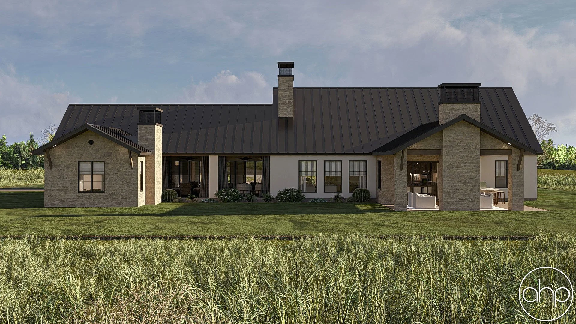 A modern house with a metal roof, stone chimneys, and large windows, surrounded by green grass and a field of tall grass in the foreground.