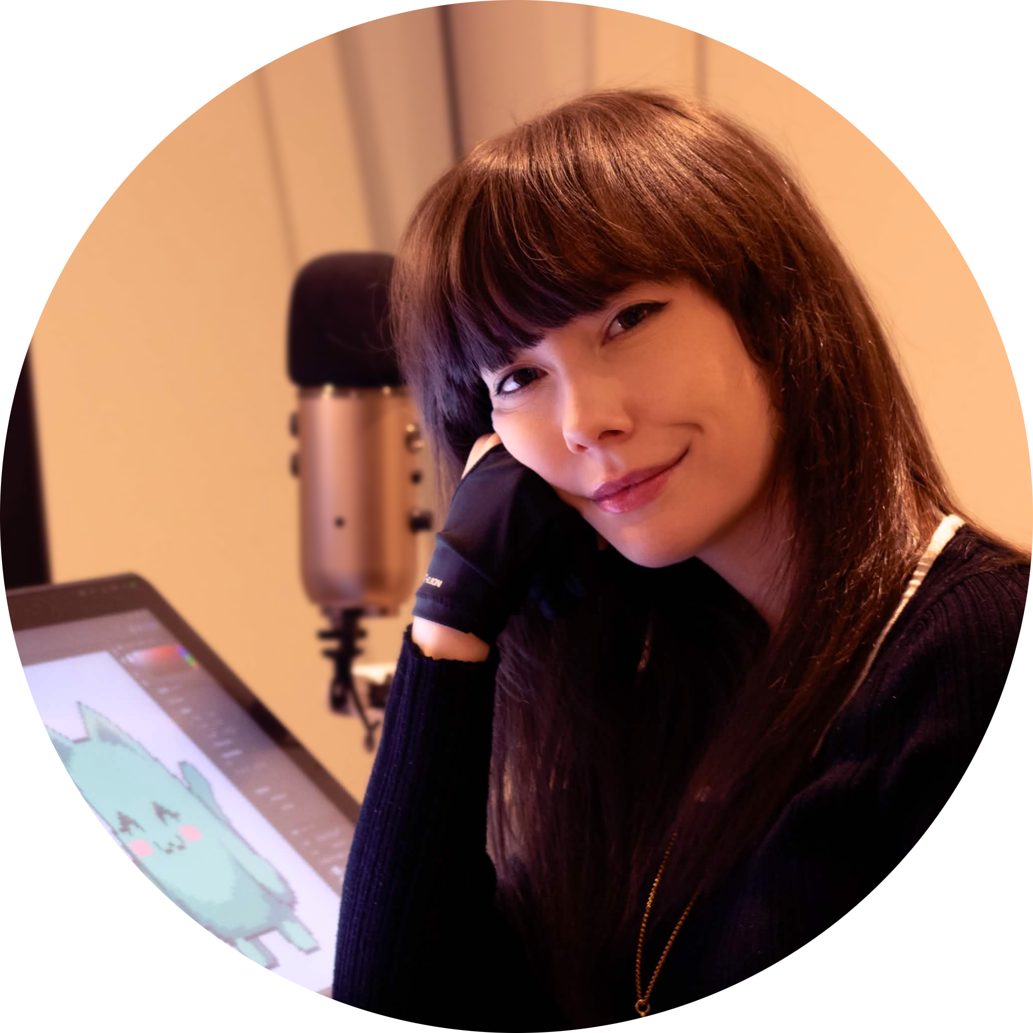 A woman with long brown hair and bangs, smiling and resting her face on her hand, in a recording or streaming setup with a microphone and drawing tablet showing a cartoon character.