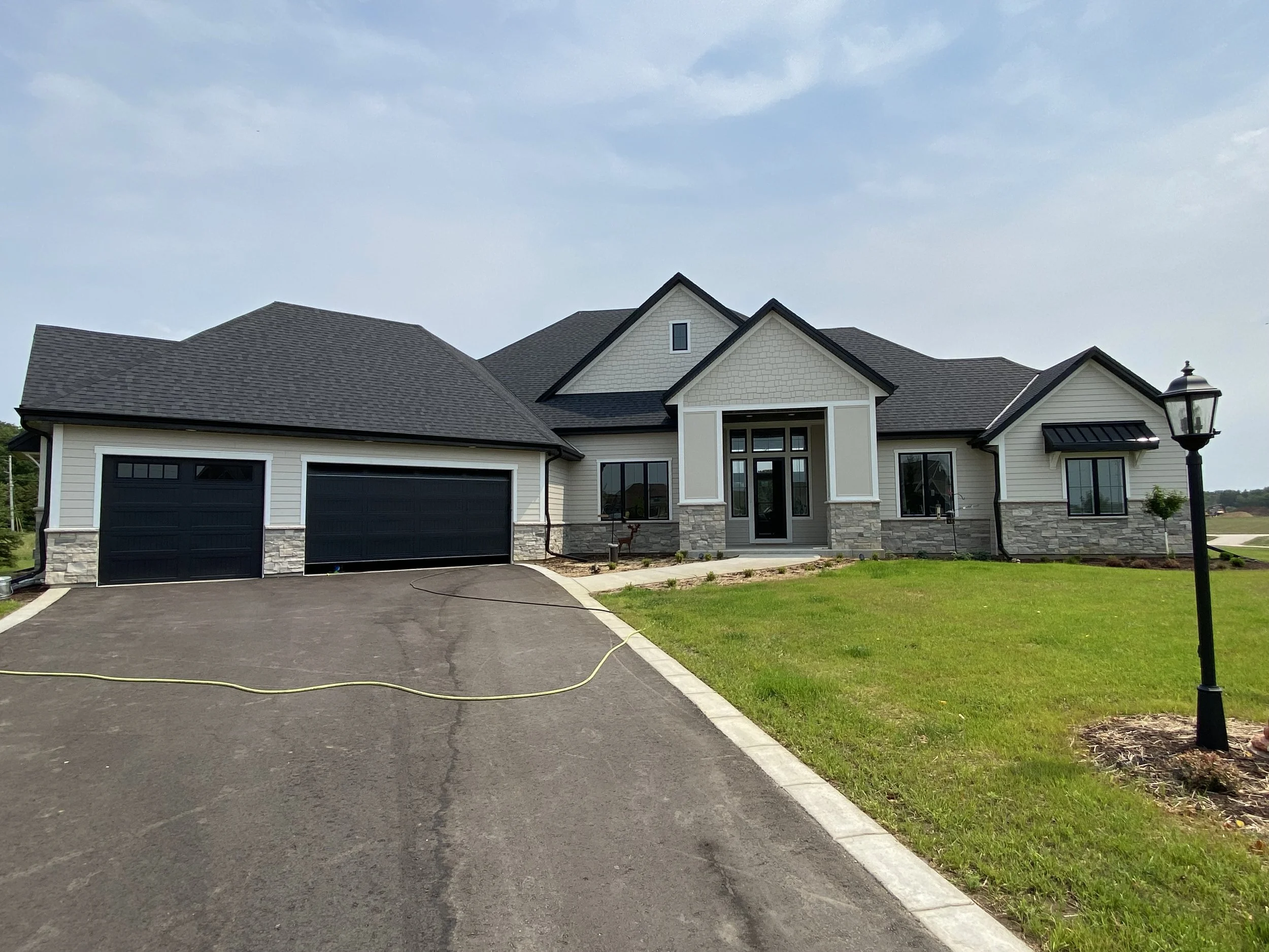 Large modern house with a stone and siding exterior, dark roof, attached garage, and a front yard with green grass, a lamp post, and sidewalks leading to the entrance.