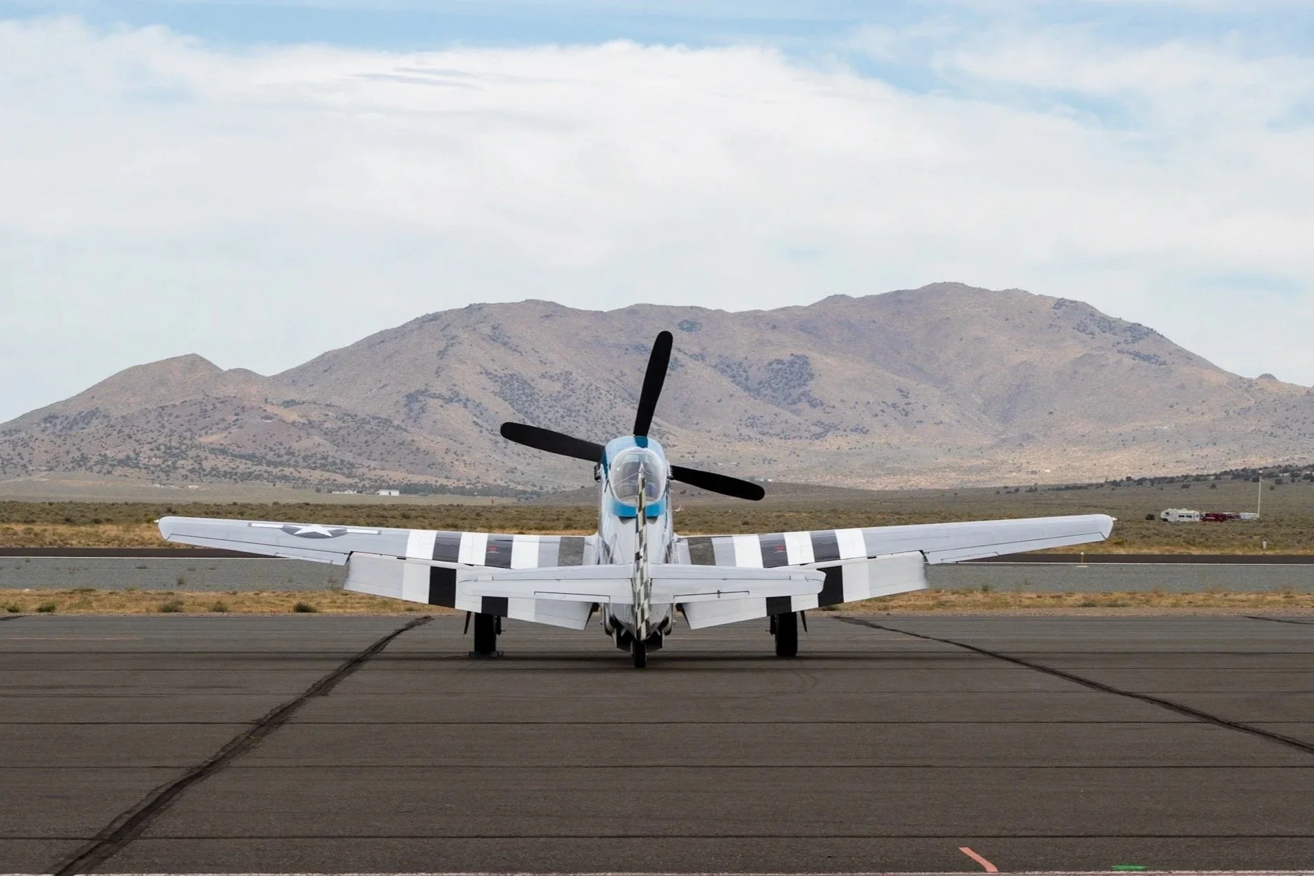 A vintage military aircraft on an airstrip with a mountain range in the background.