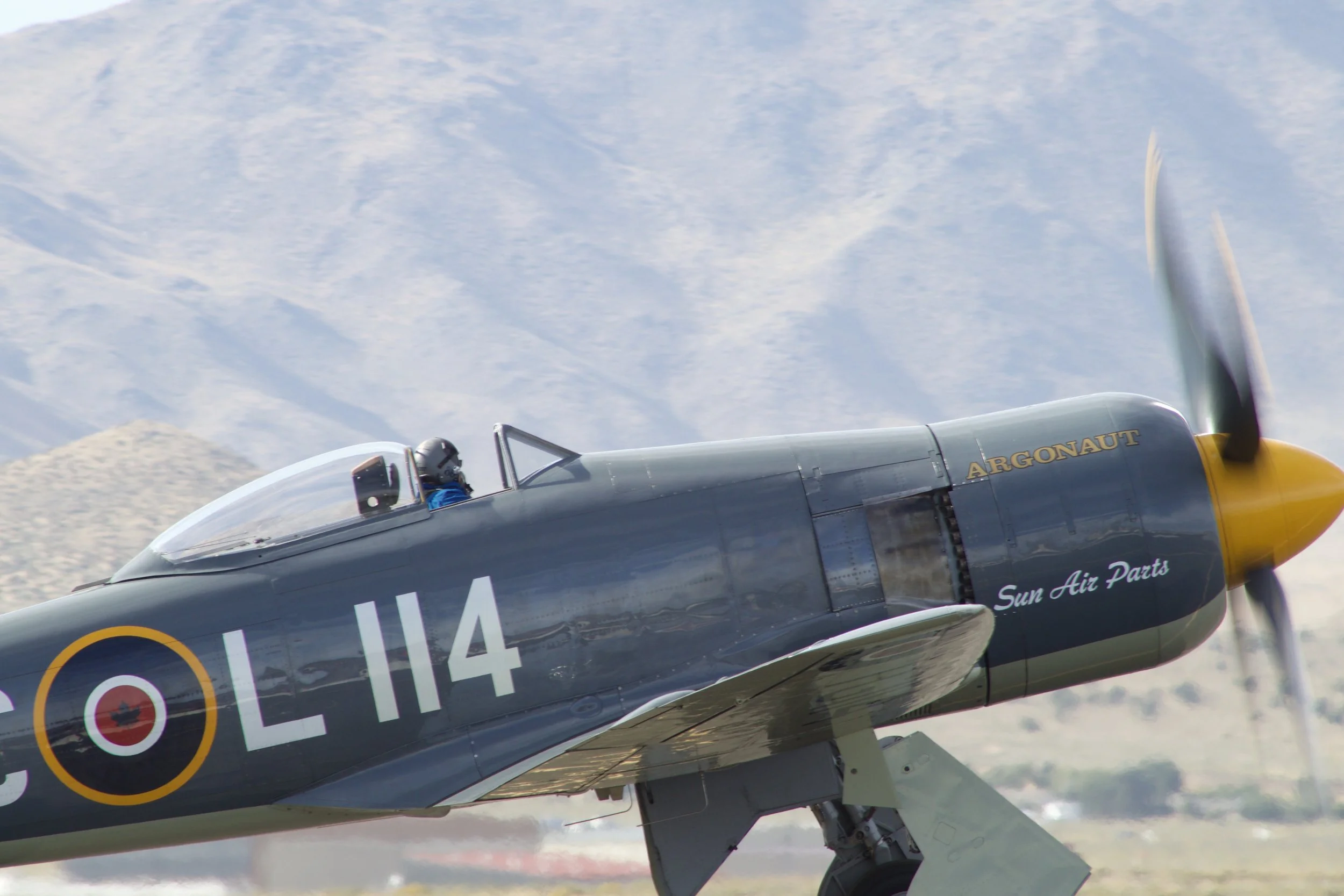 A vintage fighter plane with the words "ARGONAUT" and "Sun Air Parts" on its nose, flying in a clear sky.