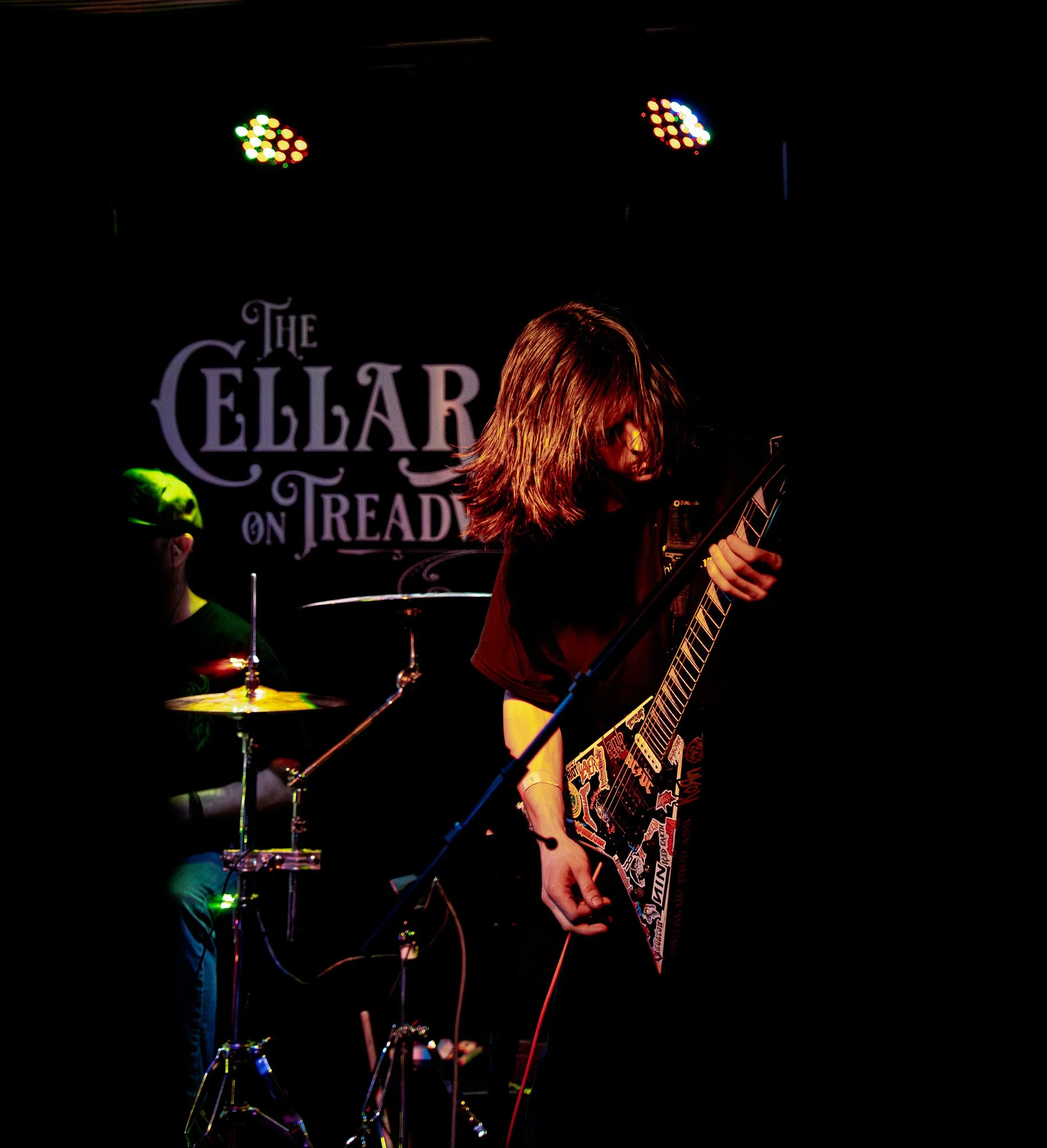 A female guitarist performing on stage with a dark background and colorful stage lights.