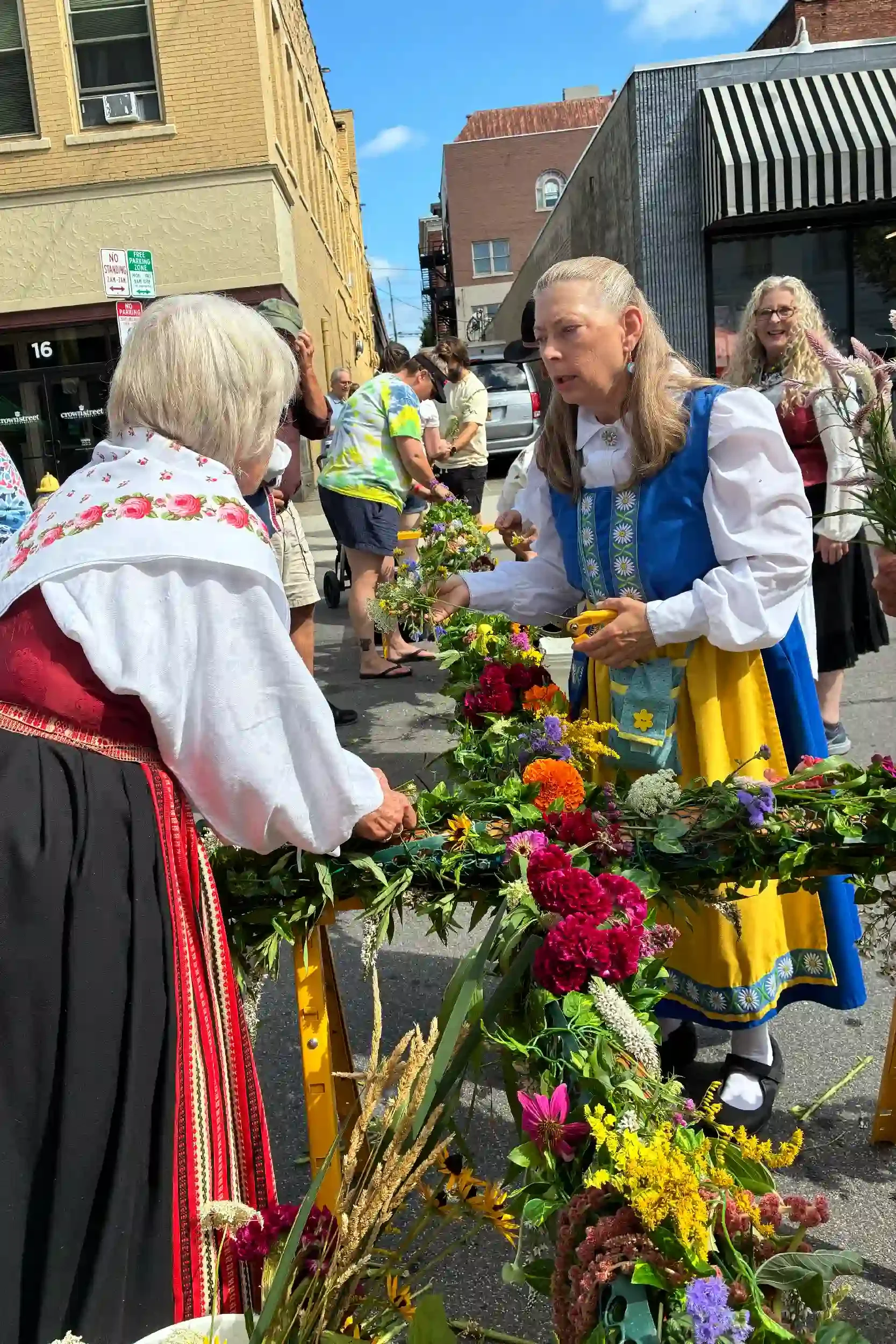 People participating in a flower market, with women dressed in traditional attire, exchanging flowers on a city street.