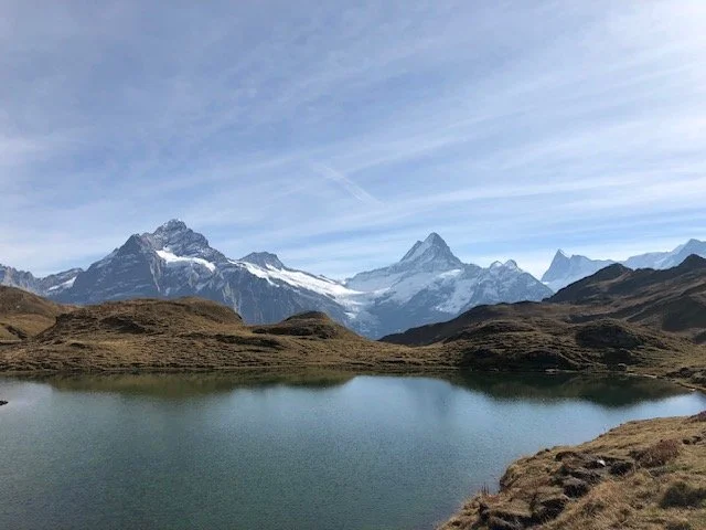 Scenic view of a mountain range with snow-capped peaks, a lake in the foreground, and a partly cloudy sky.