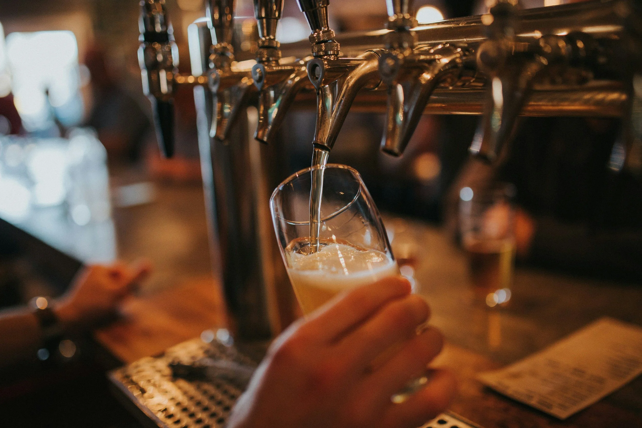 A close-up of a person pouring beer from tap handles into a glass at a bar.