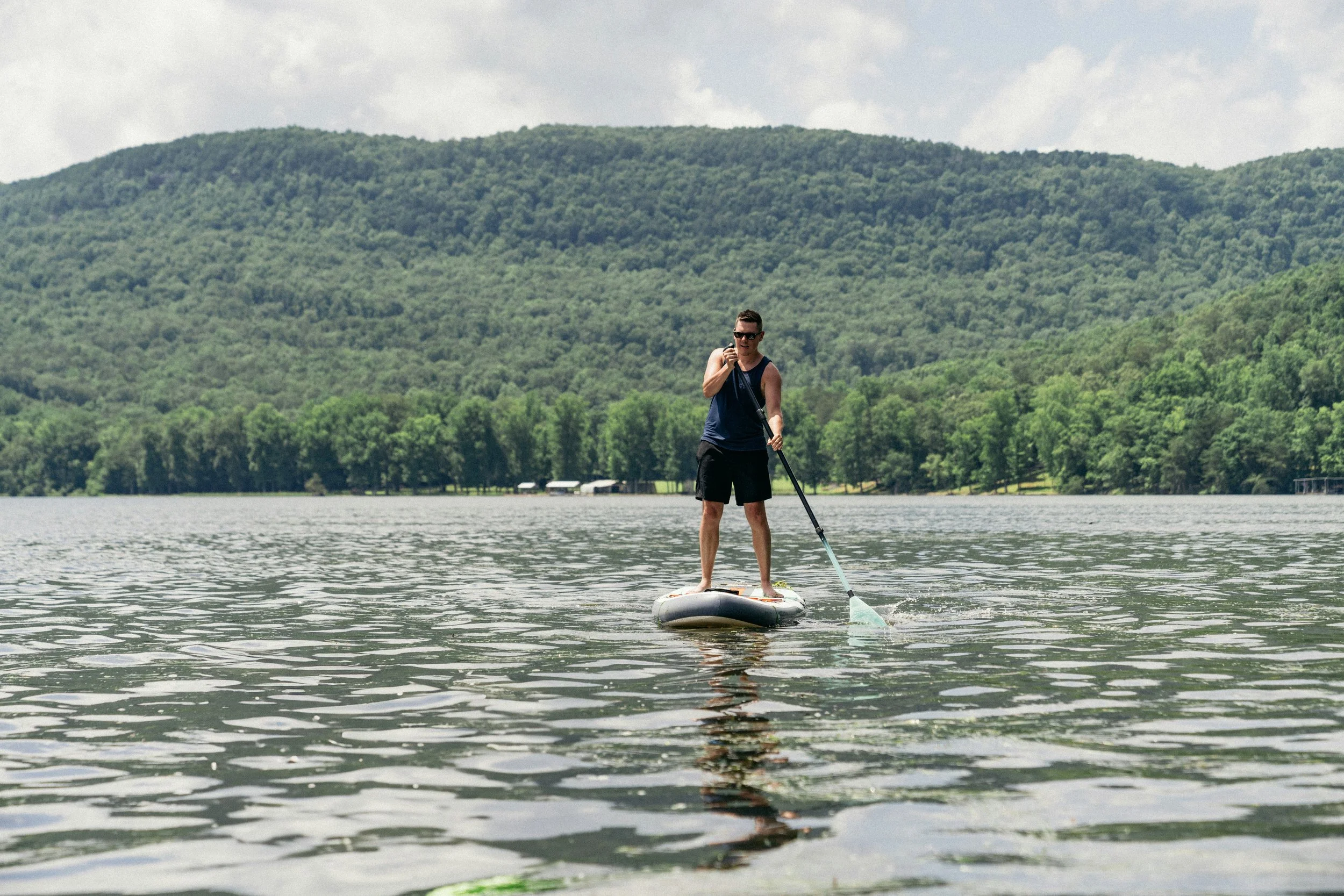 Person paddleboarding on a lake with lush green mountains in the background.
