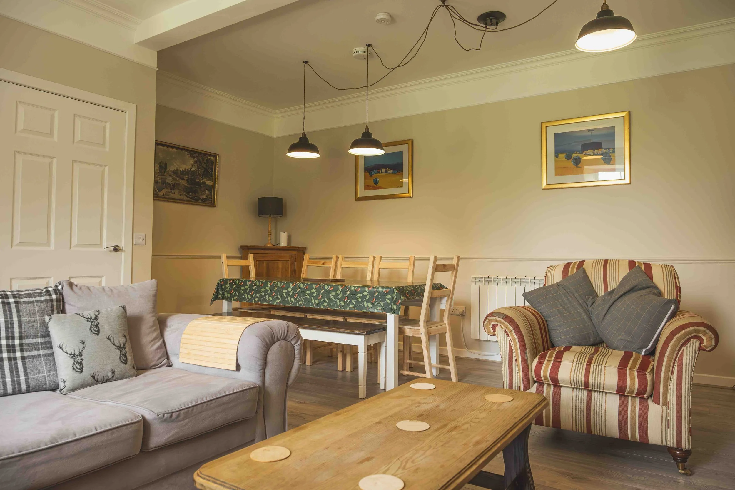 Living room with sofas, pillows, wooden coffee table, a dining table with chairs, wall art, and ceiling lights.