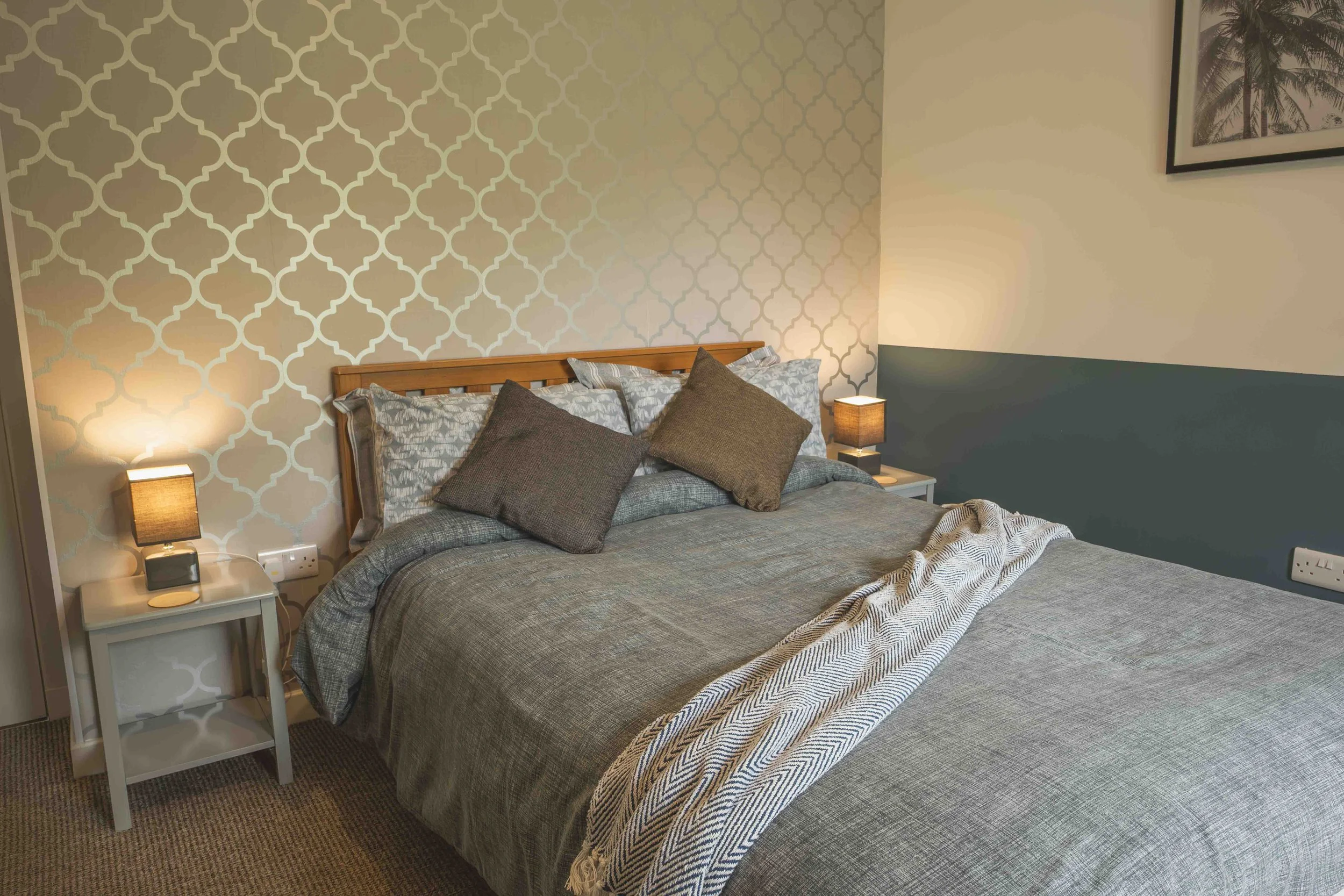 A bedroom with a bed, pillows, bedside tables with lamps, and patterned wallpaper on one wall.