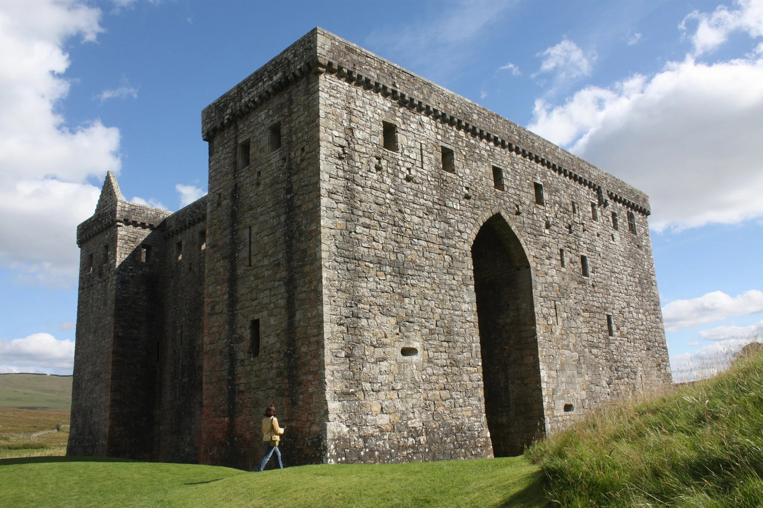 A historic stone castle with an arched entrance set in a grassy landscape under a blue sky with scattered clouds.