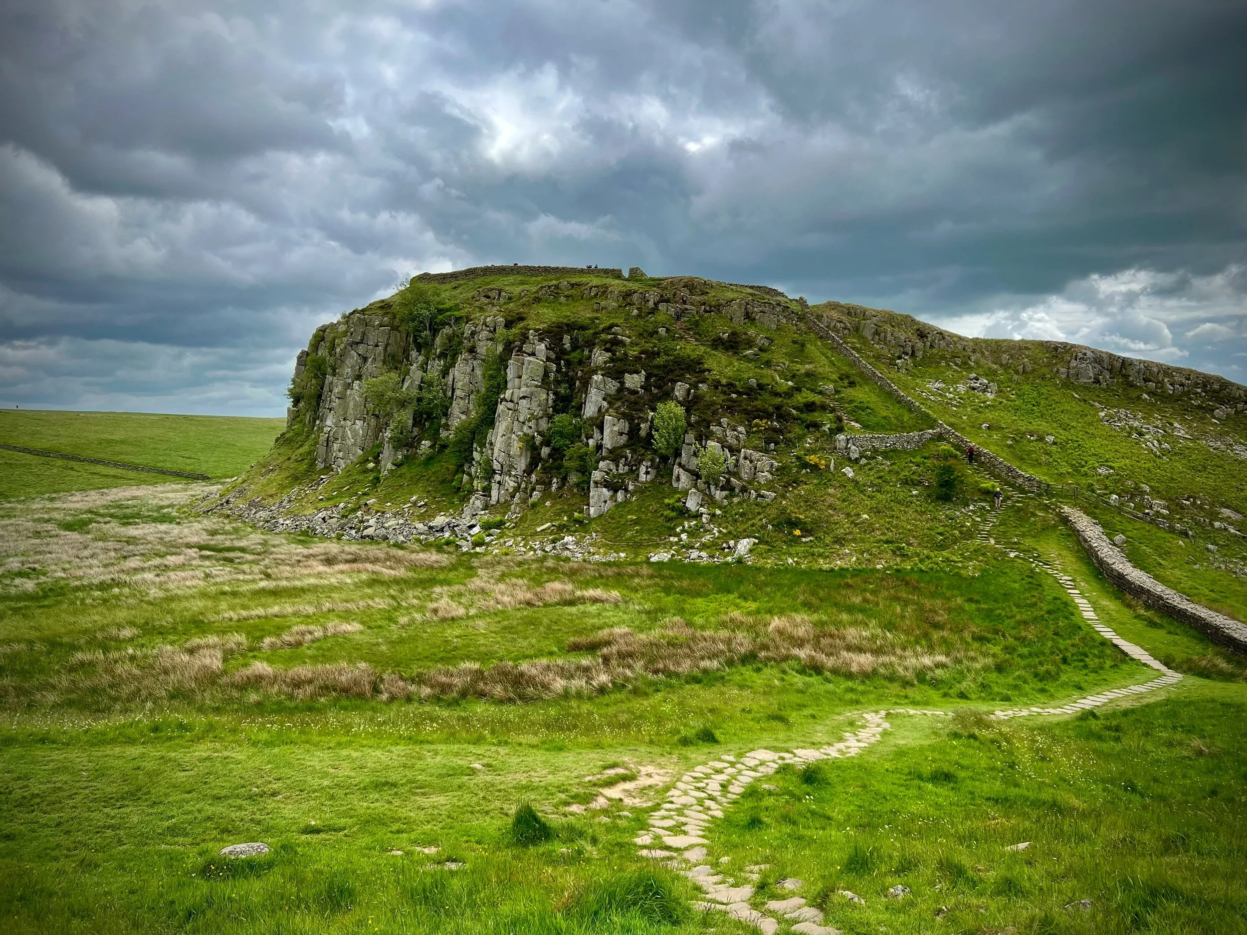 A green hill with stairs leading up to the top against a cloudy sky.
