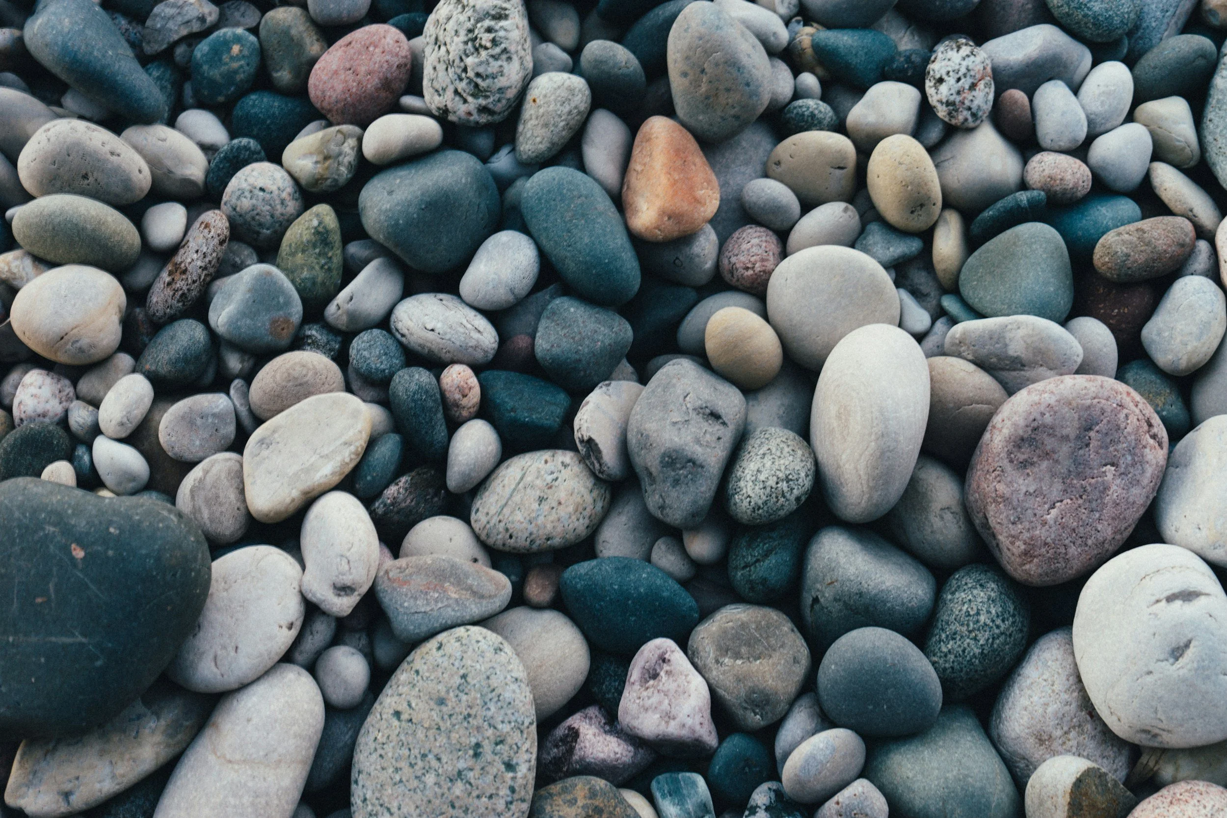 A close-up view of smooth, multicolored pebbles and stones, varying in size and shape.
