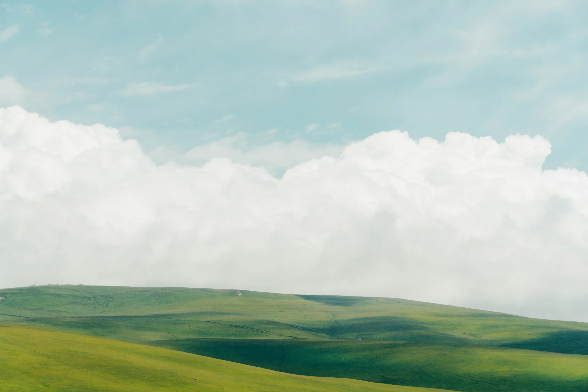 Green rolling hills under a pale blue sky with white, fluffy clouds.