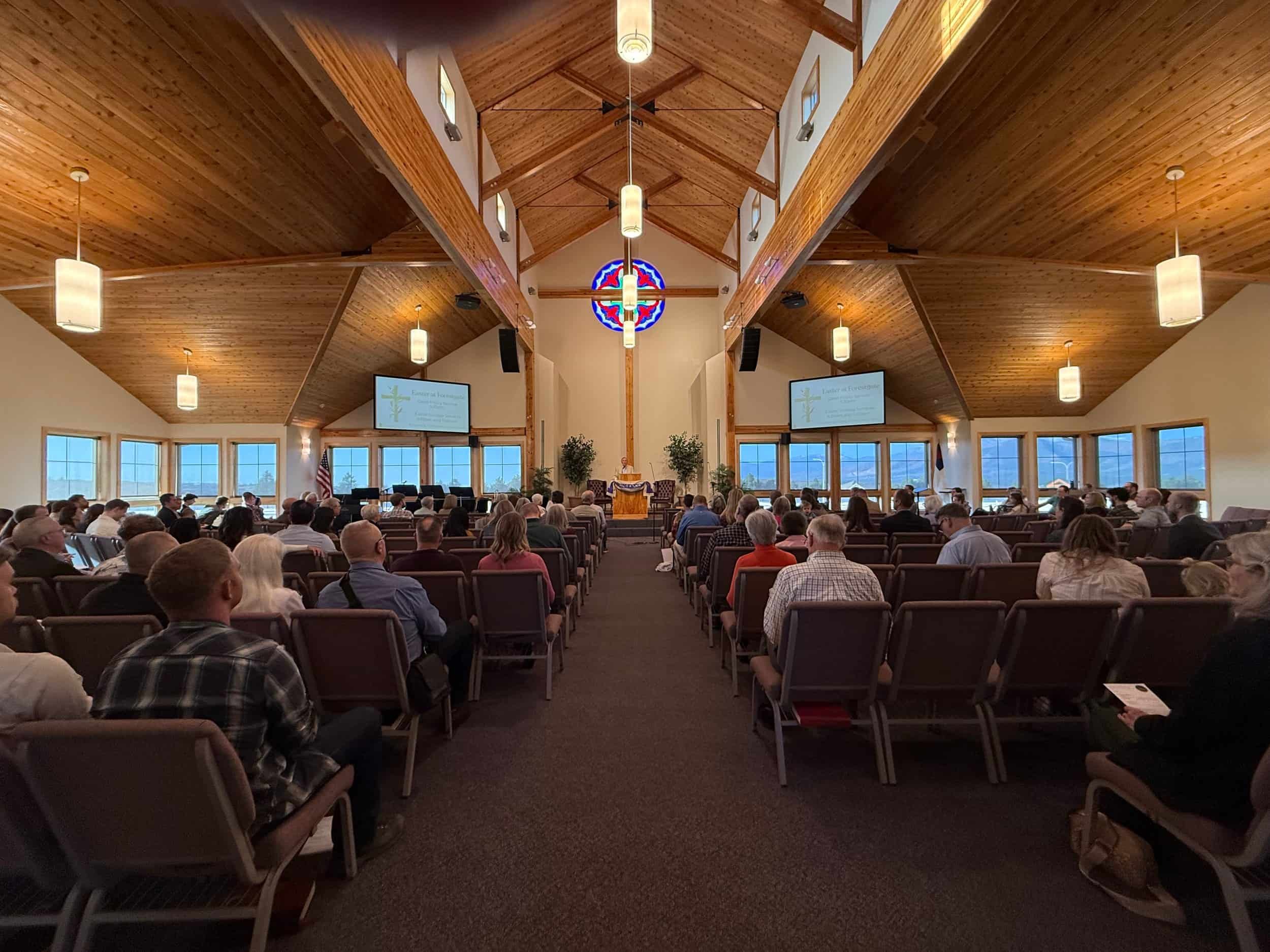 A congregation sits in rows inside Forestgate Presbyterian Church with wooden ceilings, stained glass, and screens displaying text at the front.