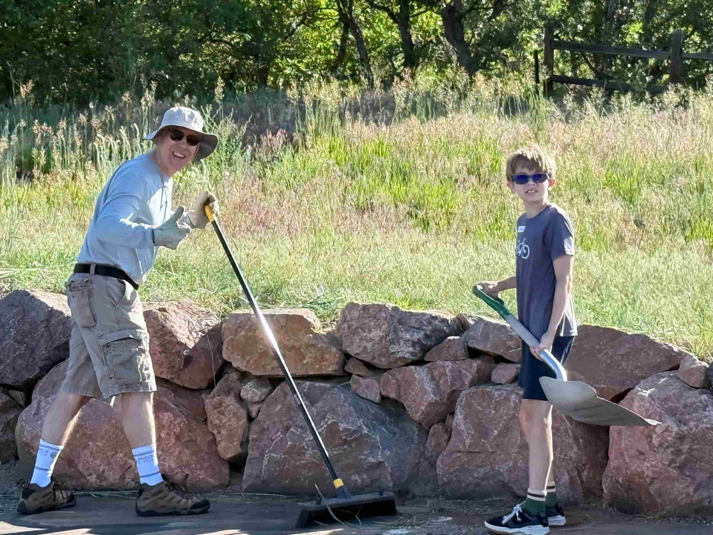 Two men with shovels and brooms cleaning.