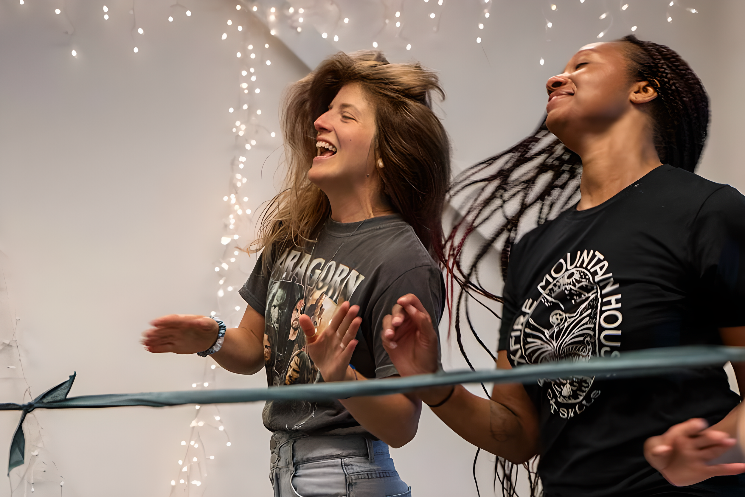 Two women are dancing and having fun, with string lights in the background.