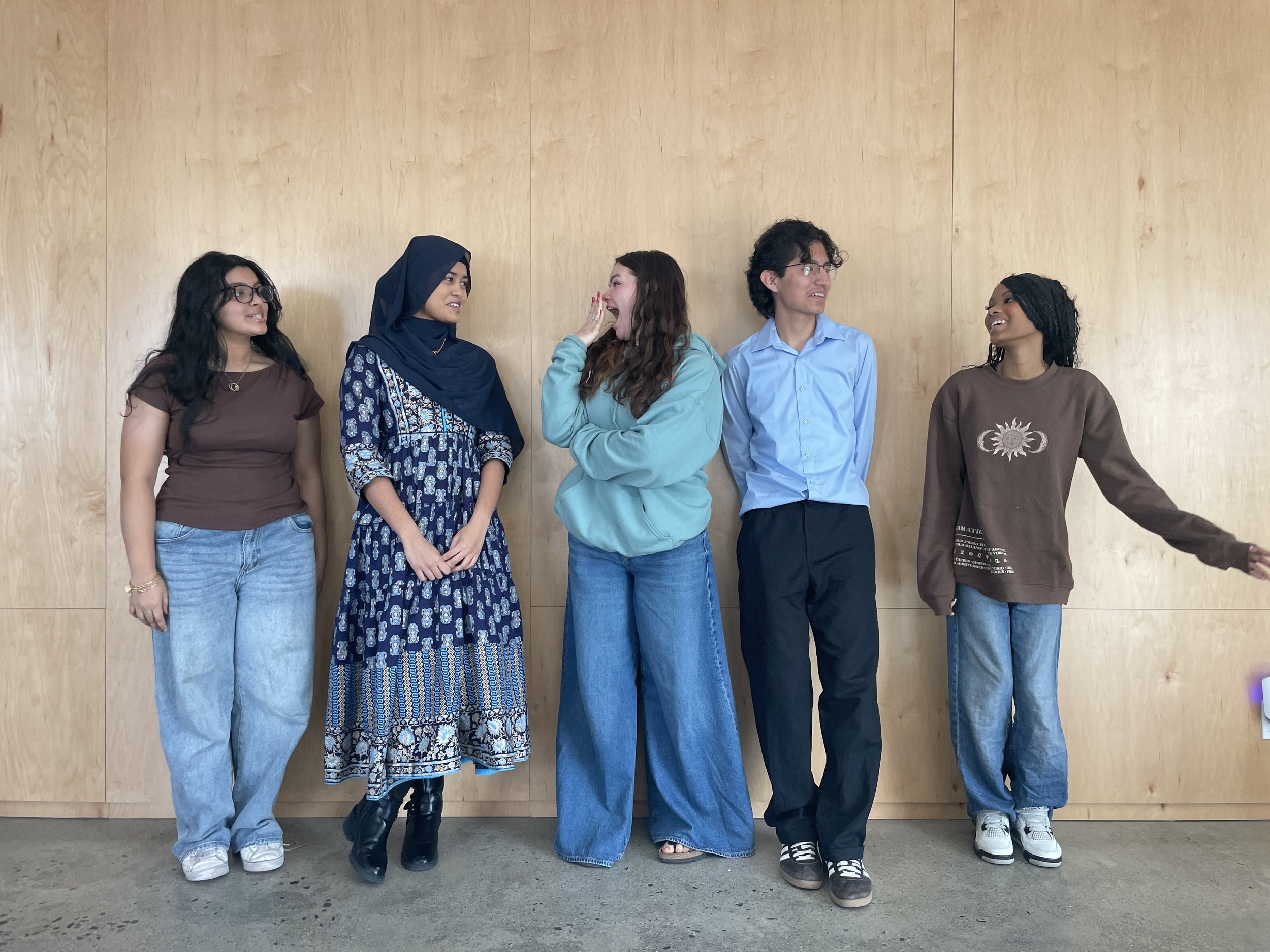 Four young women and one young man against a wooden backdrop laughing