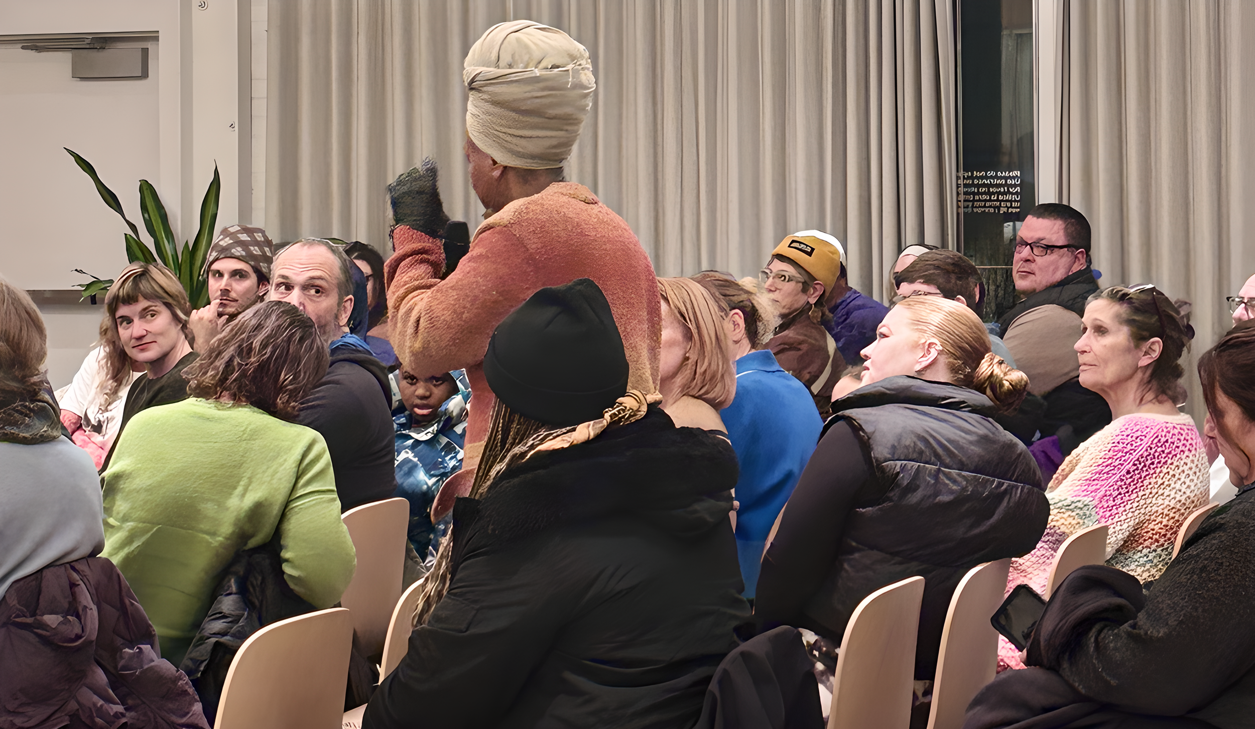 A diverse group of people sitting in chairs at a seated event, with one person standing and speaking into a microphone.