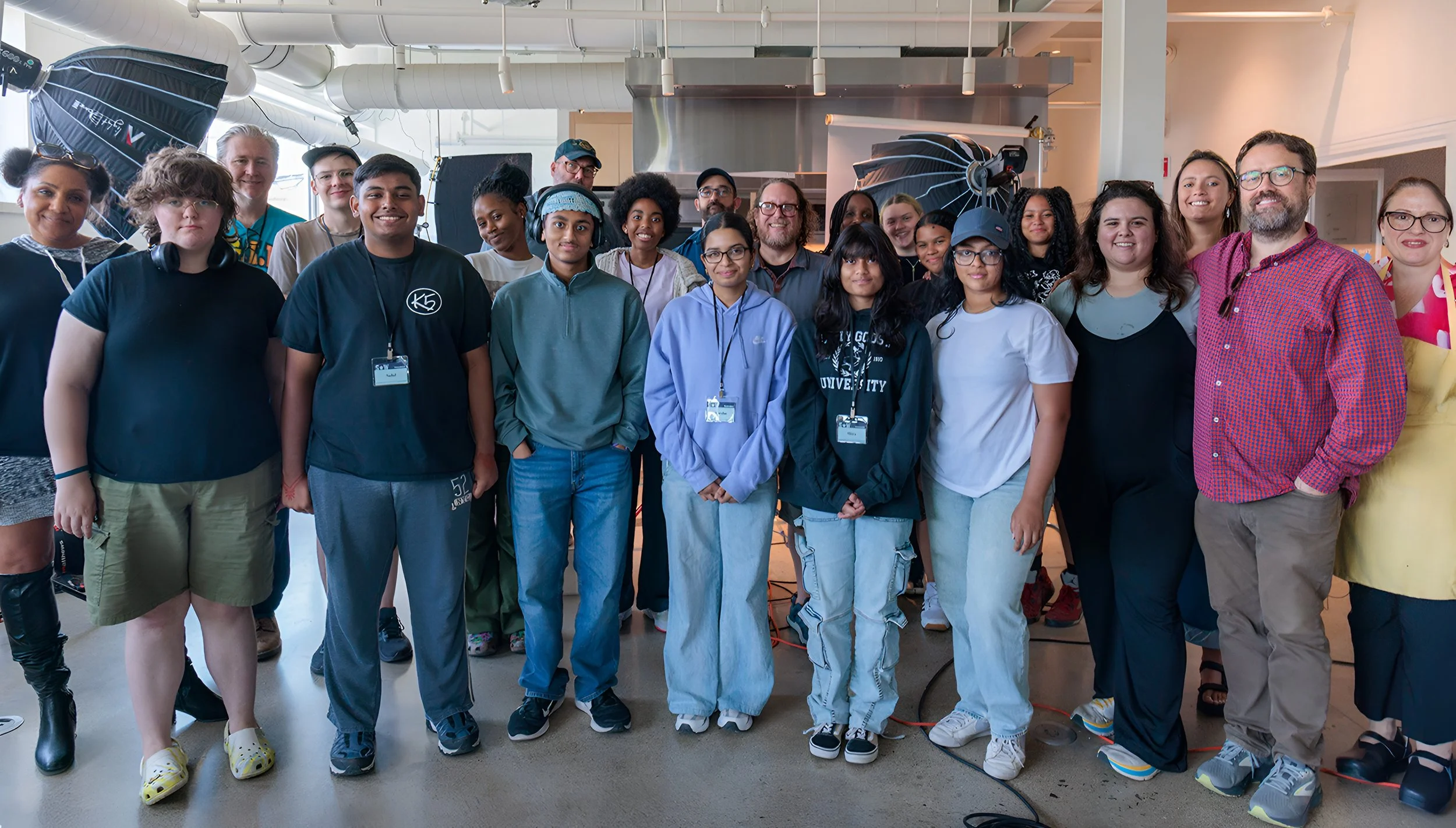 A diverse group of people posing together indoors, smiling for a photo in a professional or creative setting with photography equipment visible in the background.