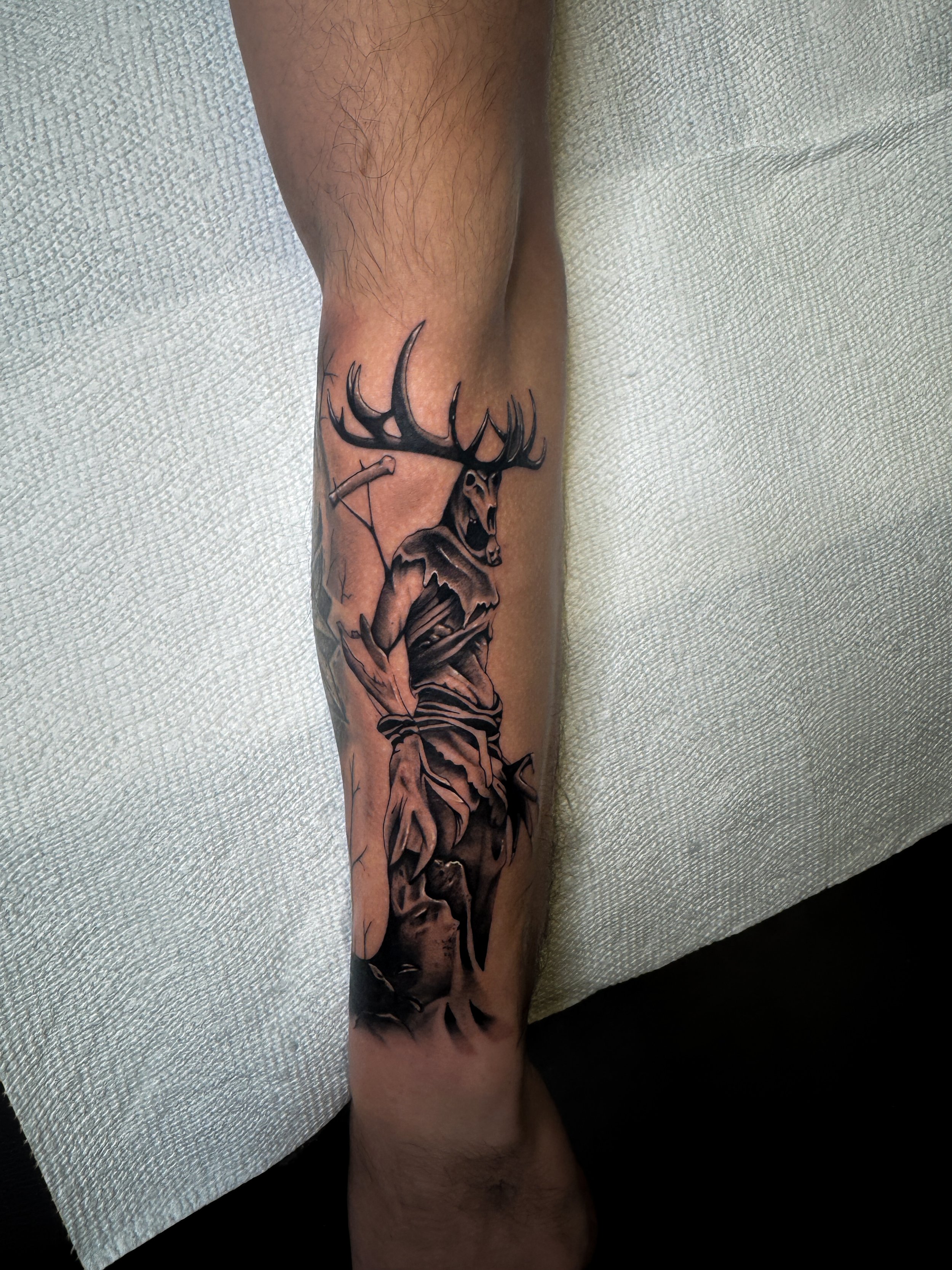 Tattoo of a man with a deer head on his shoulders, holding an arrow and bow, in black and gray in. horror tattoo realism tattoo, black and grey realism tattoo in Stuart, Sewall’s Point, Hutchinson Island, Jensen Beach, Palm City, Port St. Lucie, Fort