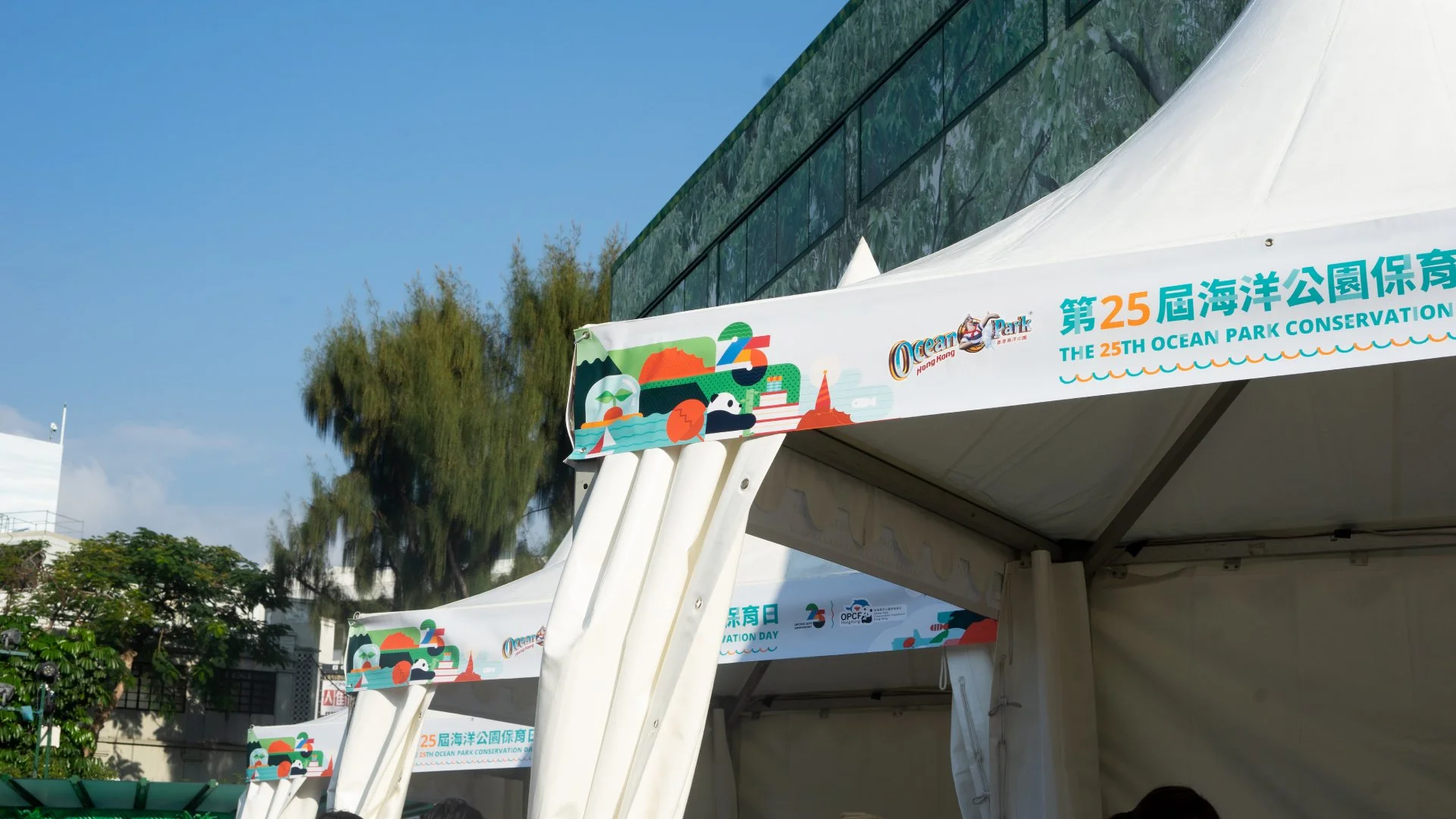 Tents with colorful banners celebrating the 25th Ocean Park Conservation Day in Hong Kong, featuring illustrations of ocean animals and nature