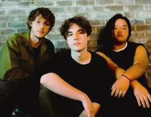 Three young men sitting in front of a brick wall, posing for the photo.