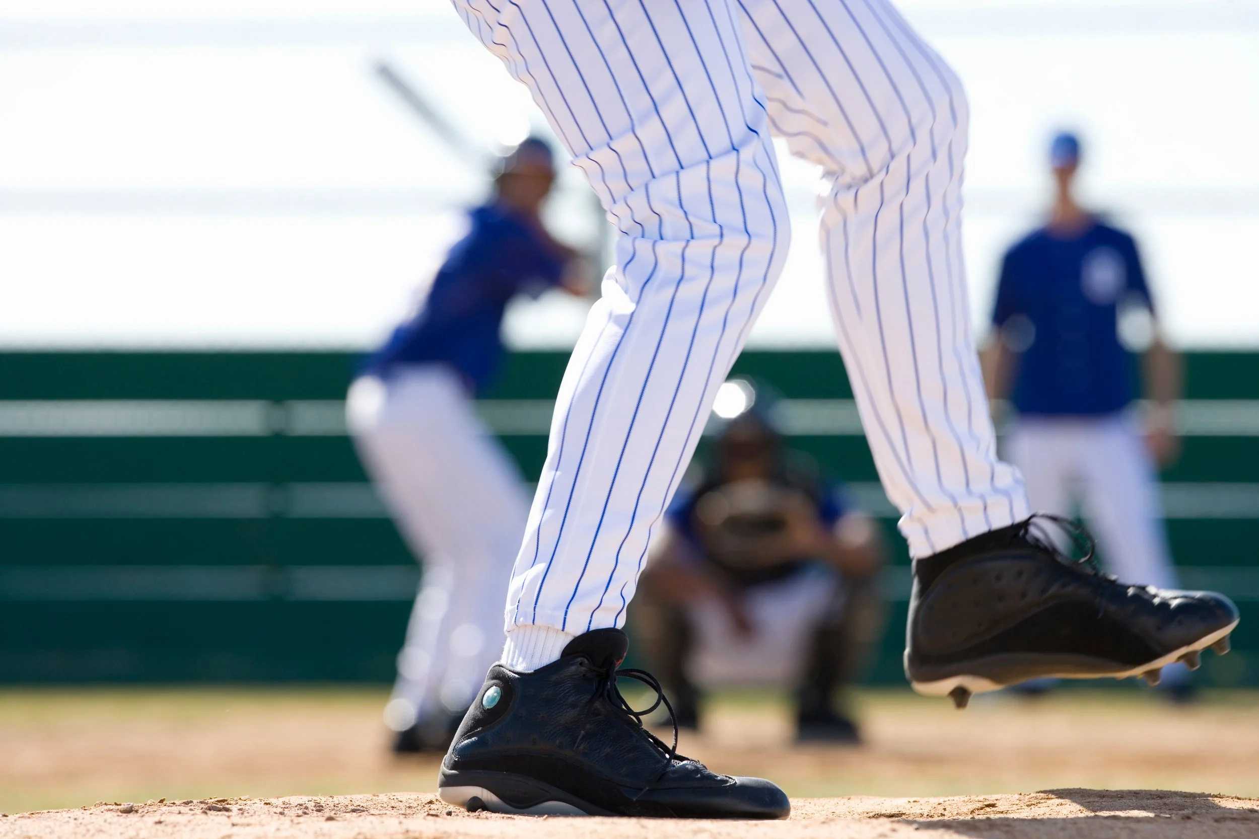 Close-up of a baseball resting on the dirt of a softball field with other baseballs in the background.