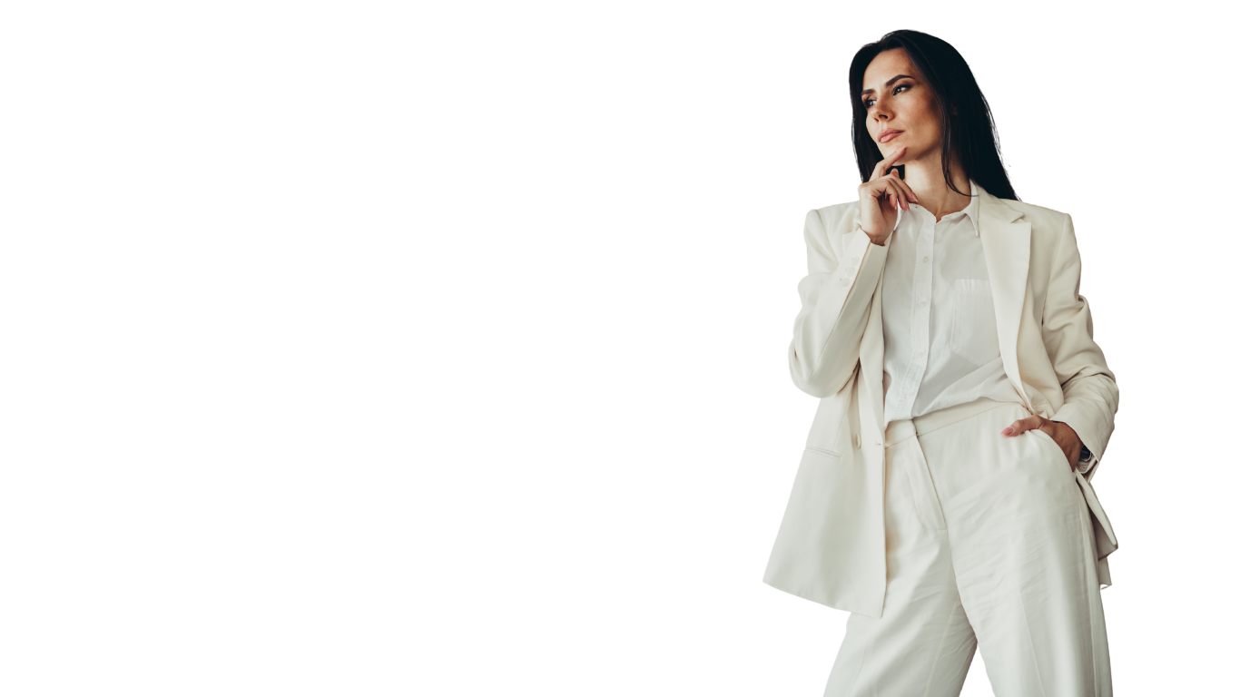 A woman dressed in a cream-colored suit, standing with one hand in her pocket and the other touching her chin, looking thoughtfully to the side.