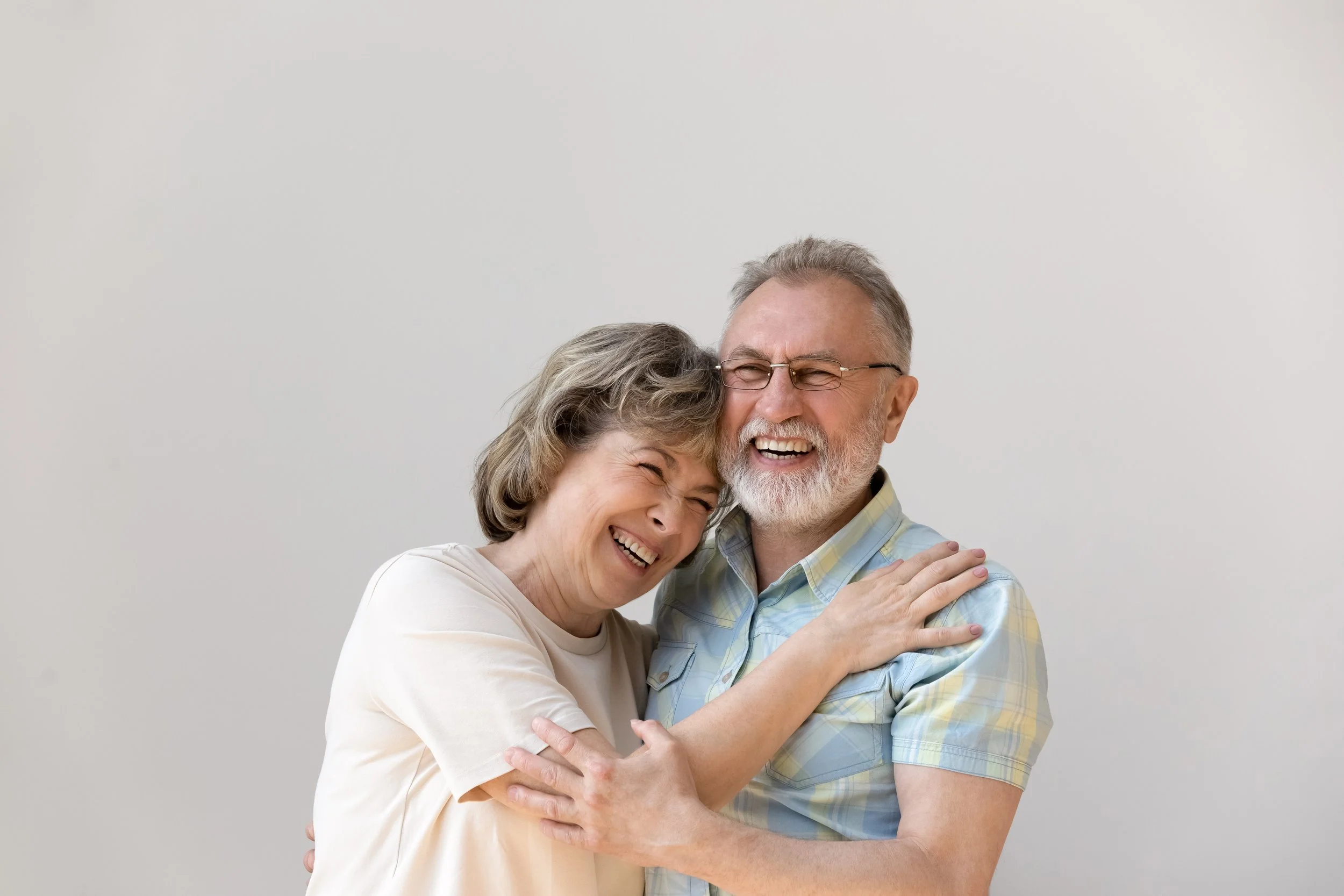 An elderly couple sharing a joyful hug and laugh against a plain white background.