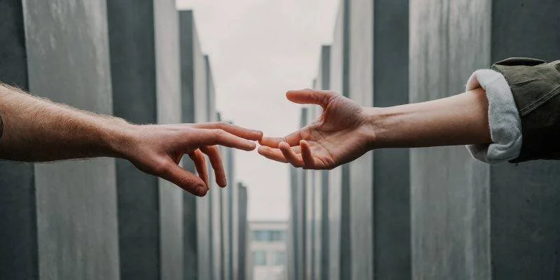 Two hands reaching out towards each other, about to touch, with a modern building corridor in the background.