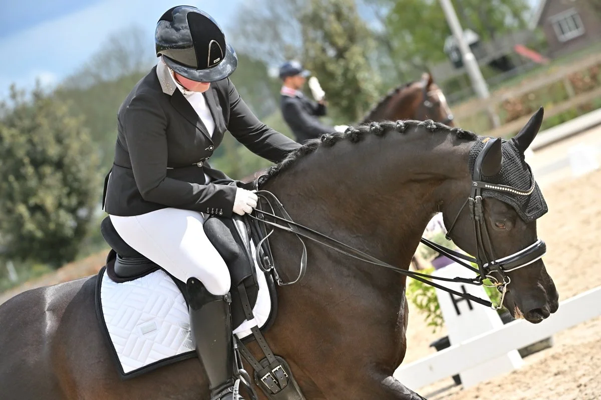A woman dressed in equestrian attire riding a horse in an outdoor arena.