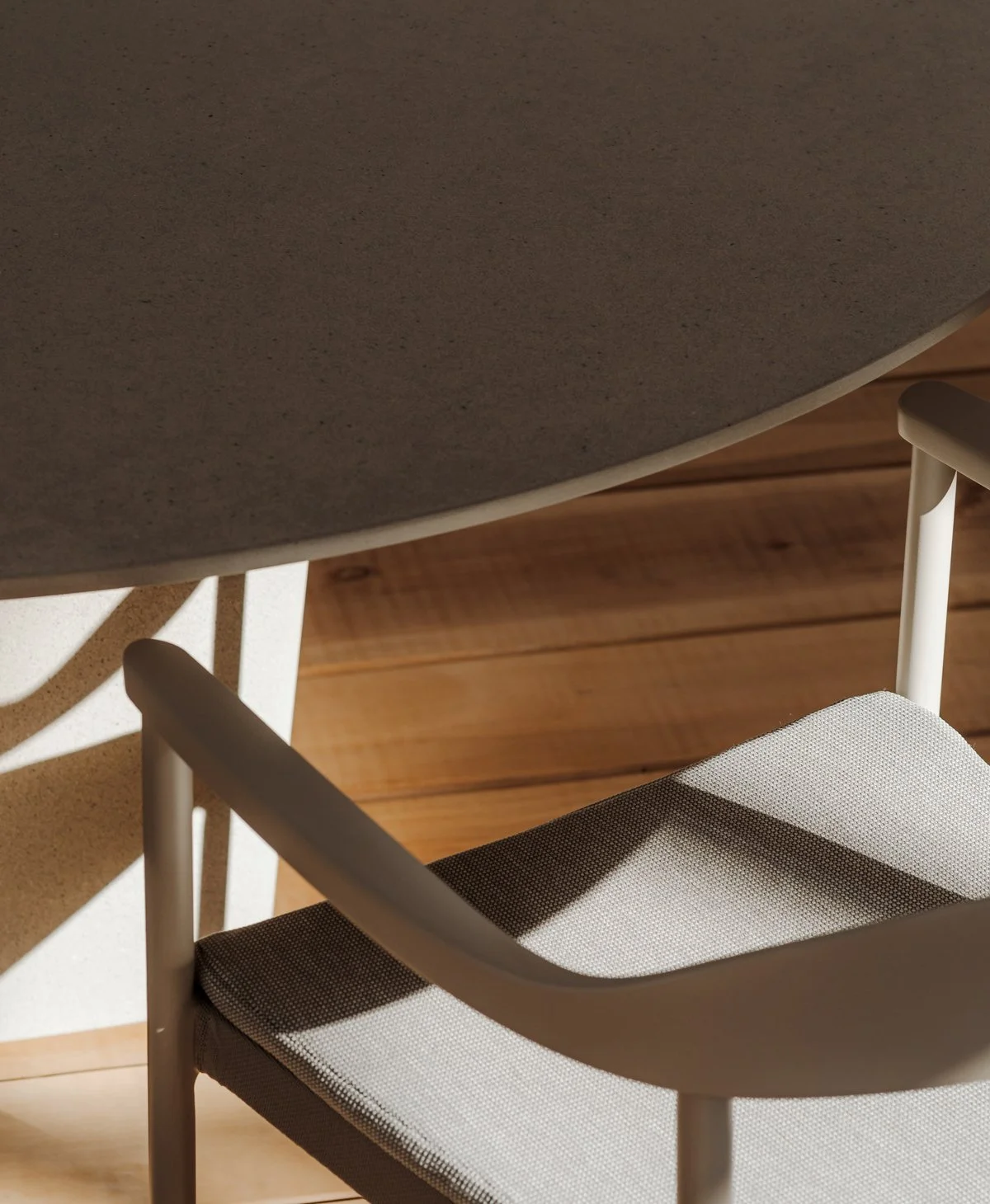 Close-up of a dining table and a chair with light-colored legs and armrests, on a wooden floor with visible planks.