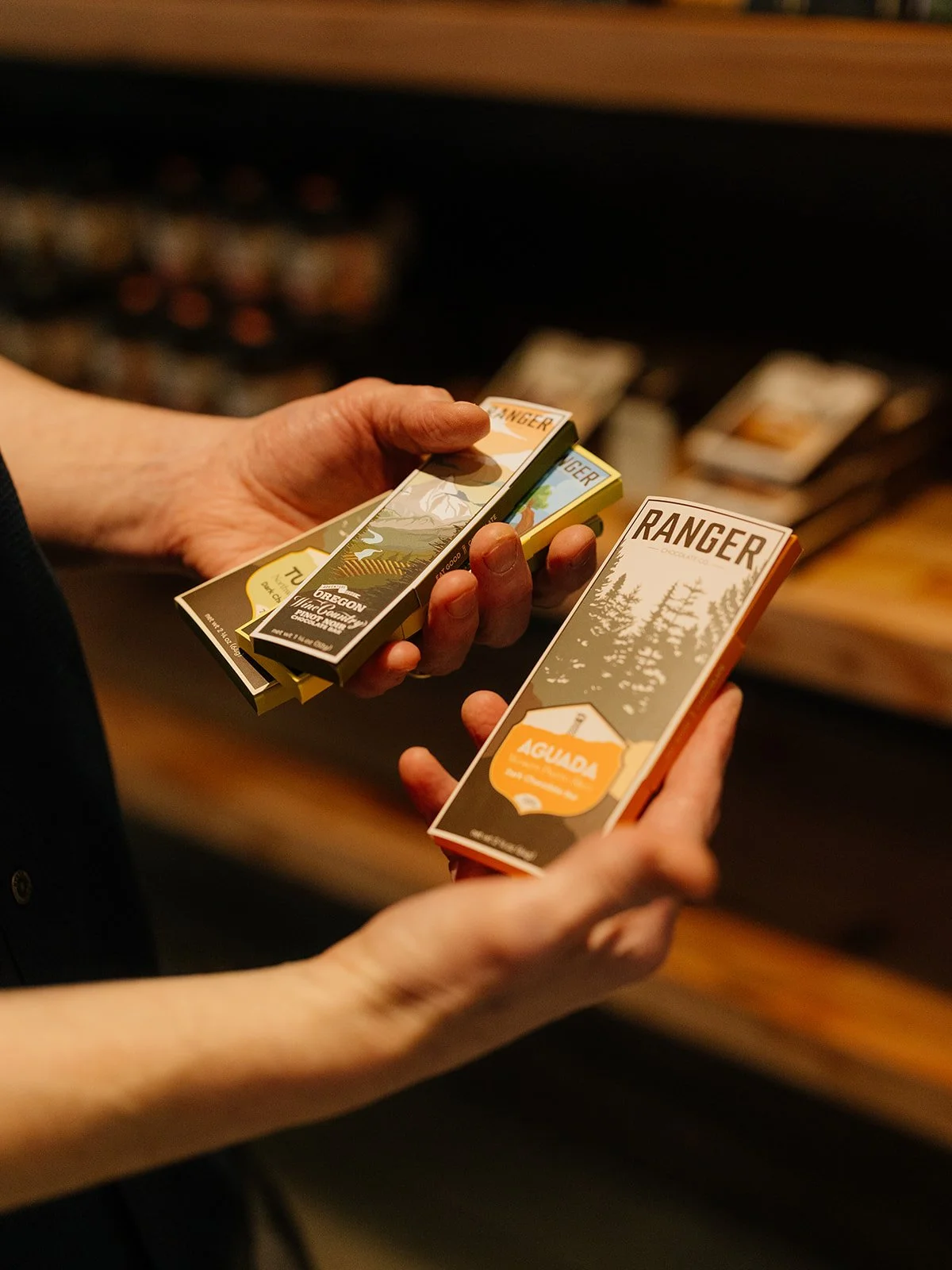Person holding small boxes of travel souvenirs with forest and mountain illustrations.