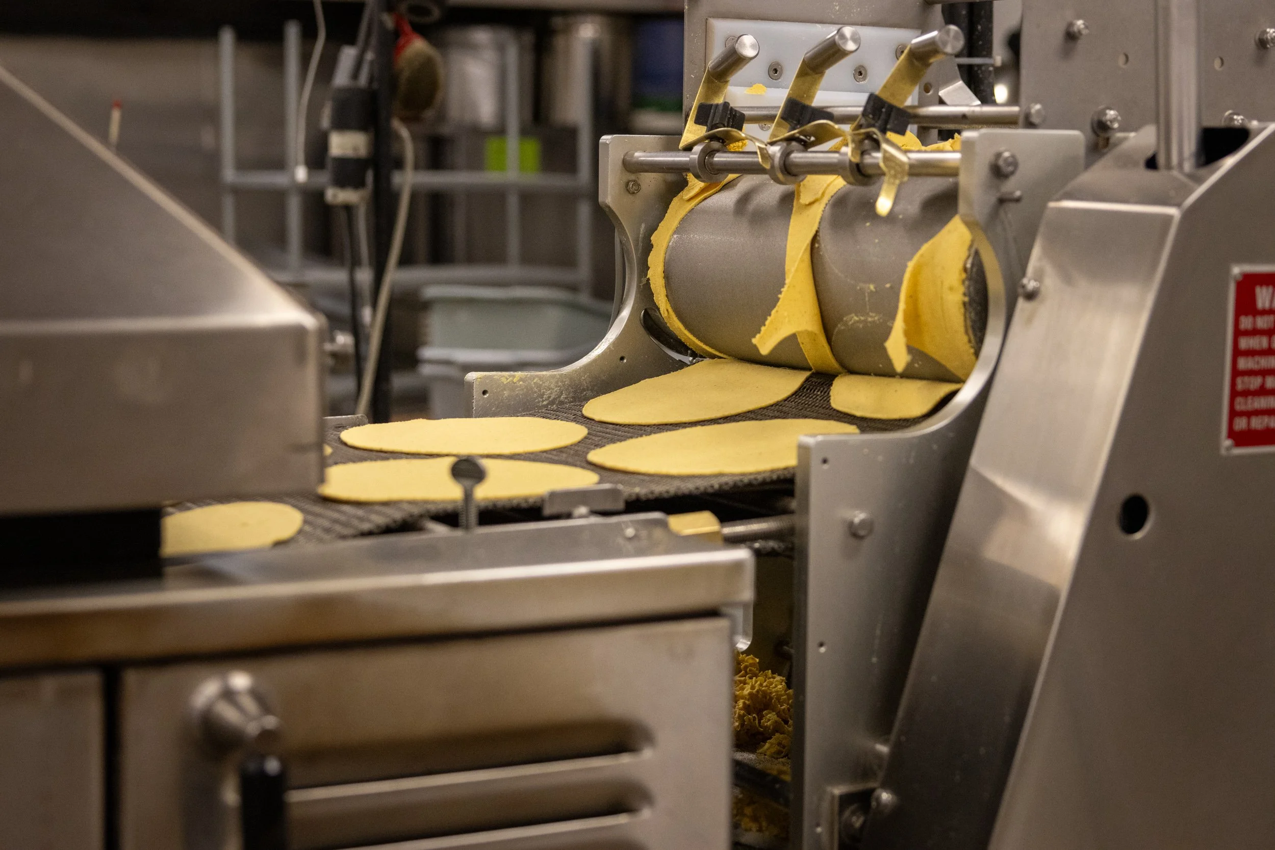 Food manufacturing machine processing yellow dough into flat circular shapes.
