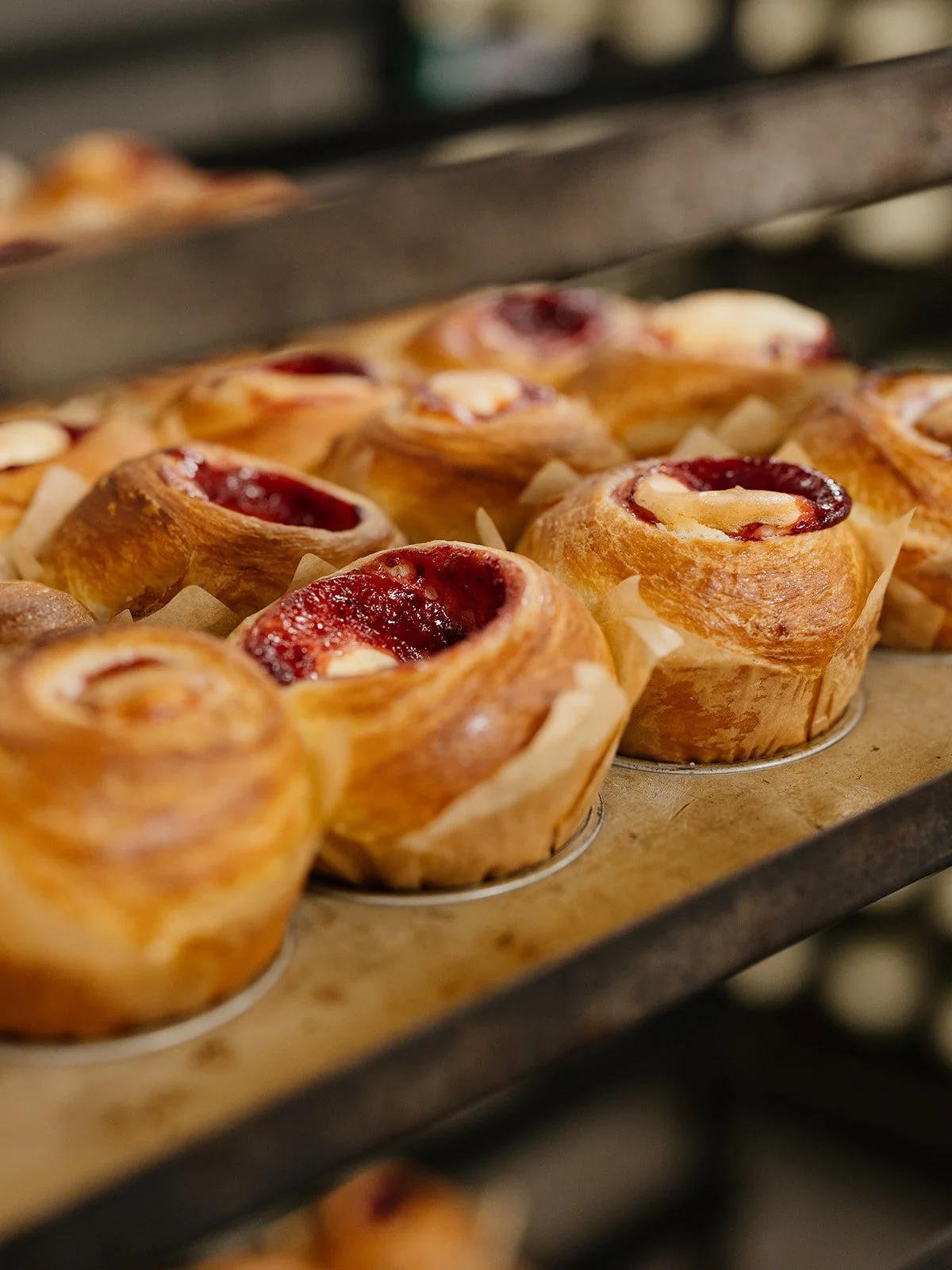 Close-up of freshly baked cinnamon rolls with red jam and cream cheese filling on a baking tray.