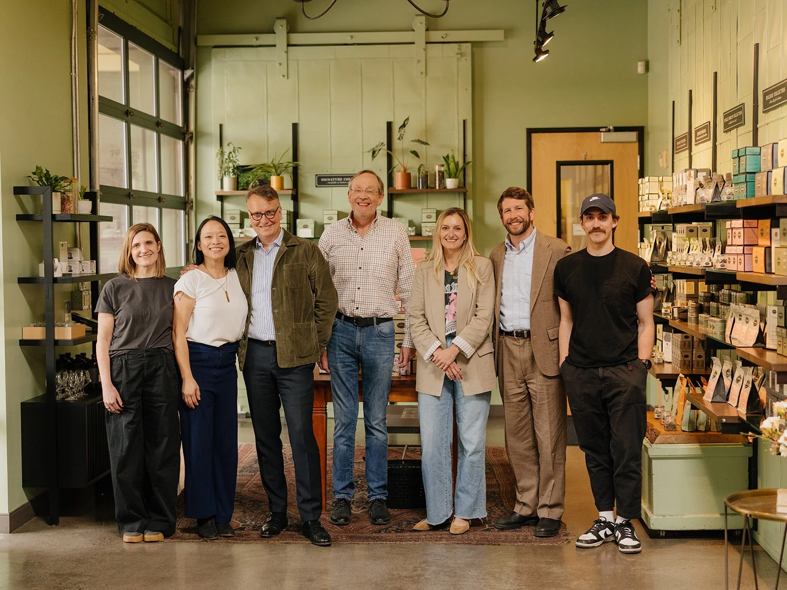 Group of seven people standing inside a retail store with green walls and shelves stocked with products.