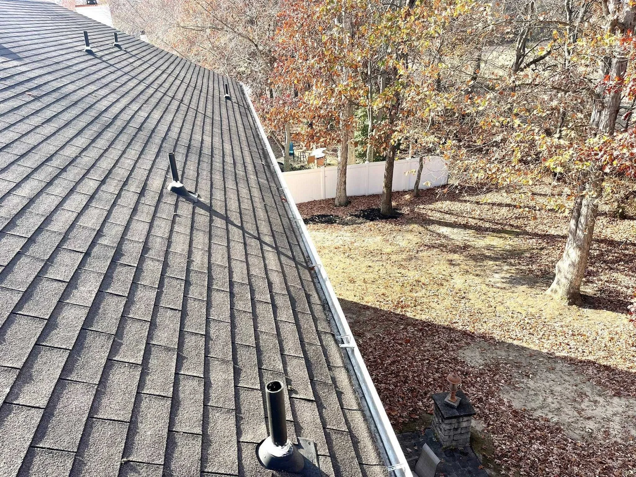 View from a rooftop showing a yard with trees shedding autumn leaves, a white fence, and a chimney