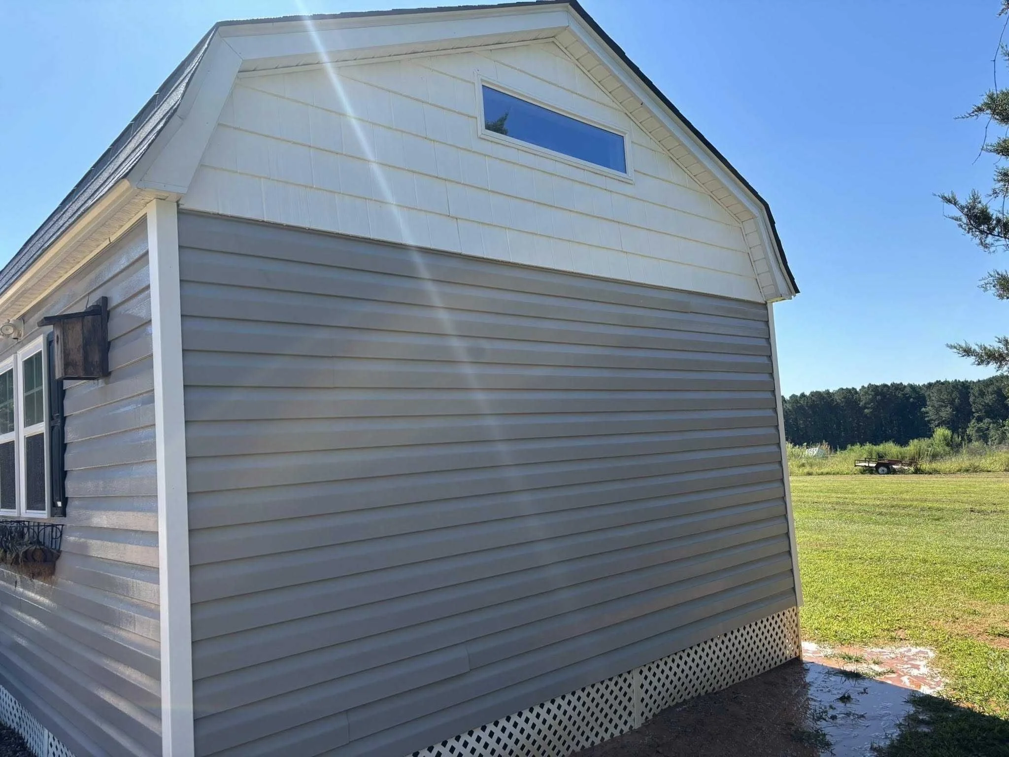 Side view of a house with vinyl siding, a small window, and a larger window with a flower box beneath it, on a sunny day with a clear blue sky.