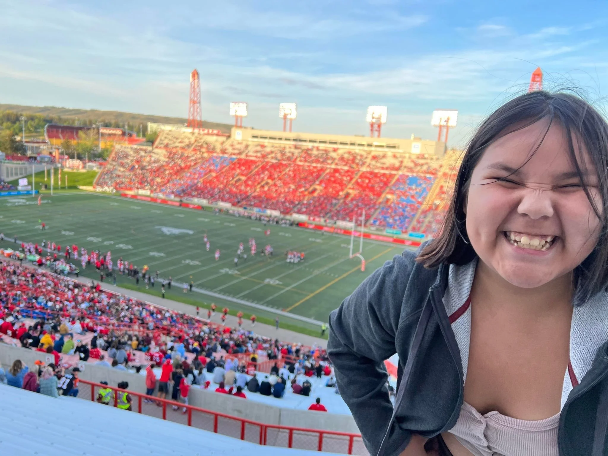 A young woman smiling happily at a football stadium filled with spectators during a game.