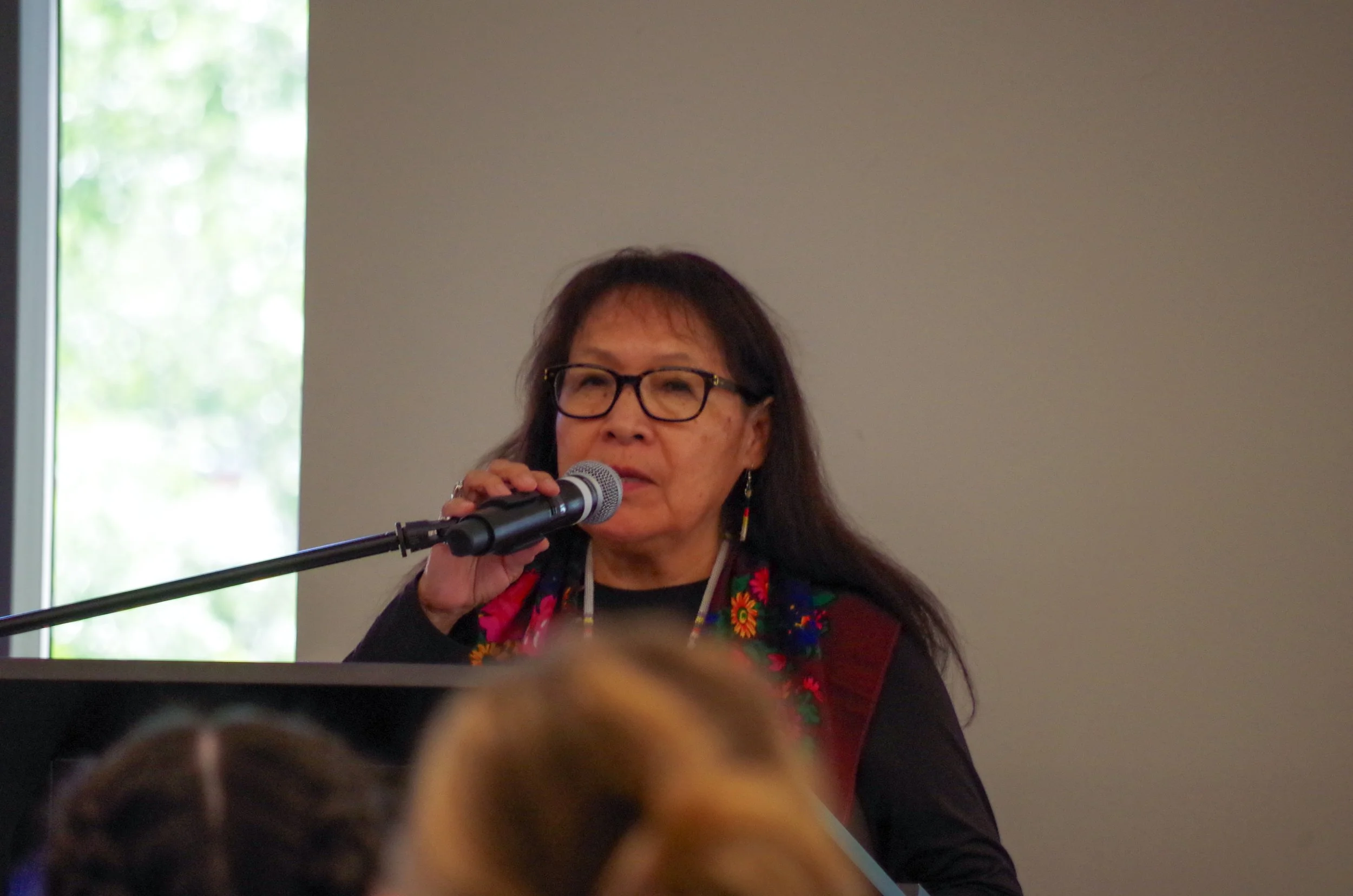 Woman with glasses speaking into microphone at event