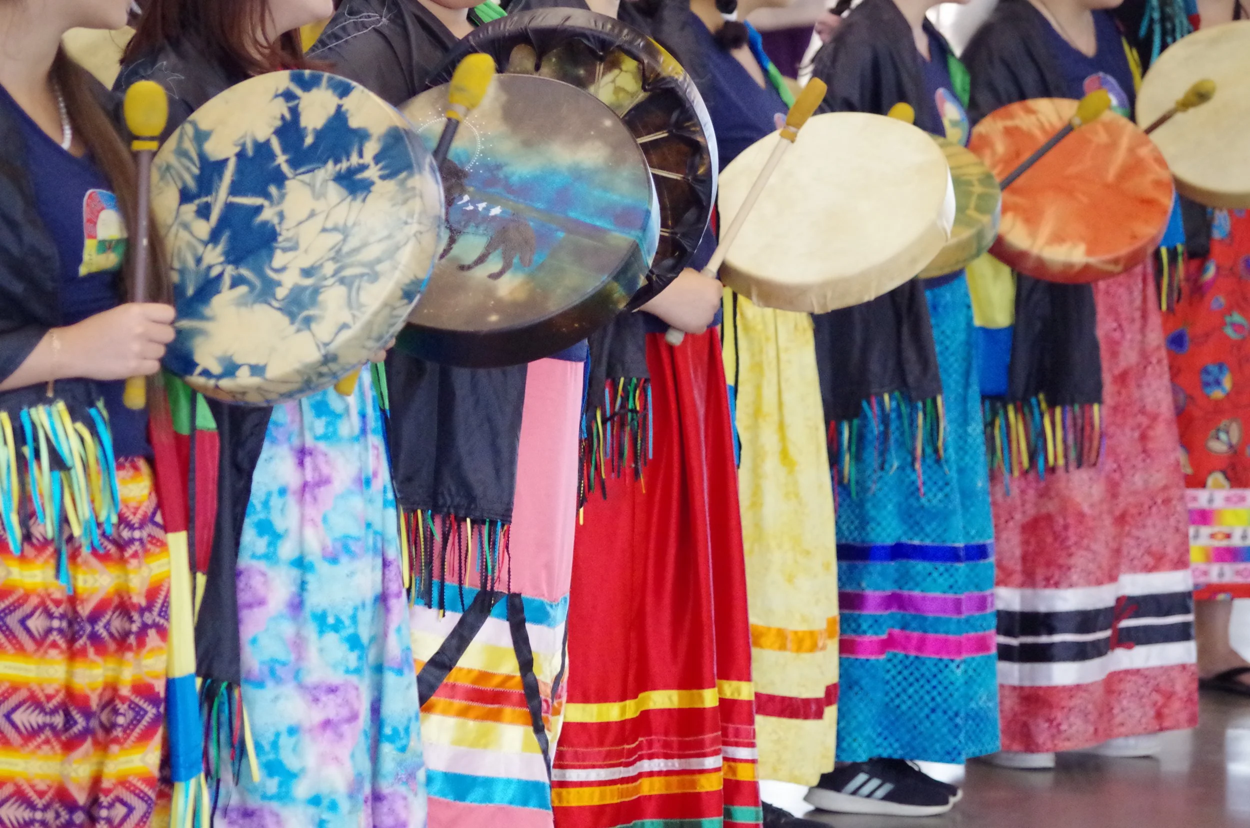 A group of women dressed in colorful traditional skirts and black tops holding various drums during a cultural performance or celebration.