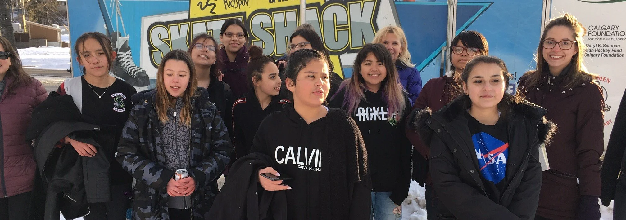 Group of young women and girls outdoors in winter, posing in front of a colorful bus with 