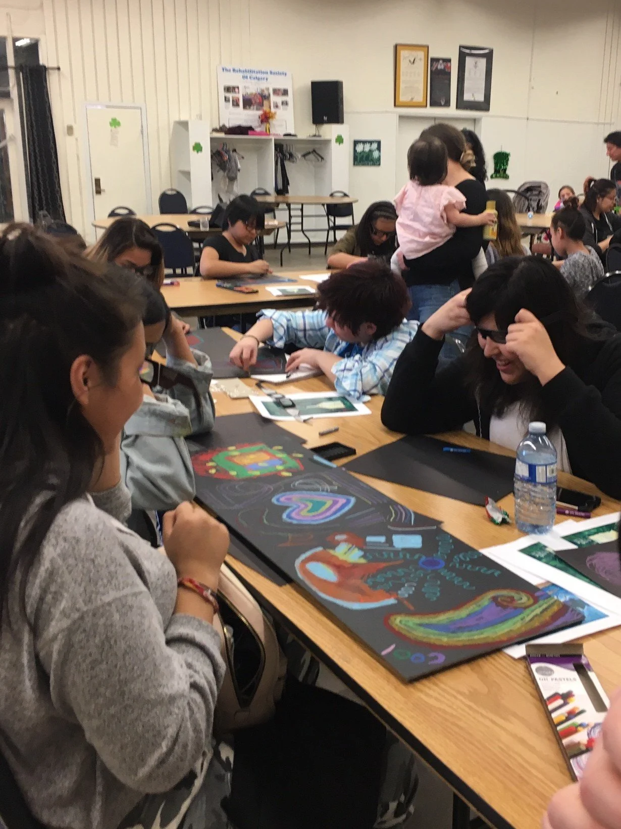 A classroom with students working on colorful chalkboard art projects at tables, engaging in creative activities.